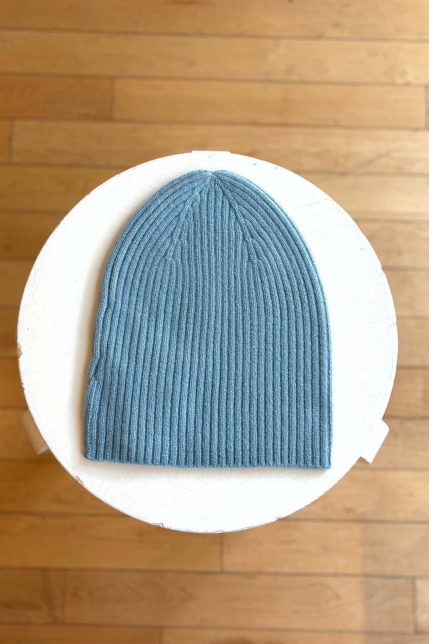 Light blue knit beanie on a white circular platform with a wooden floor background