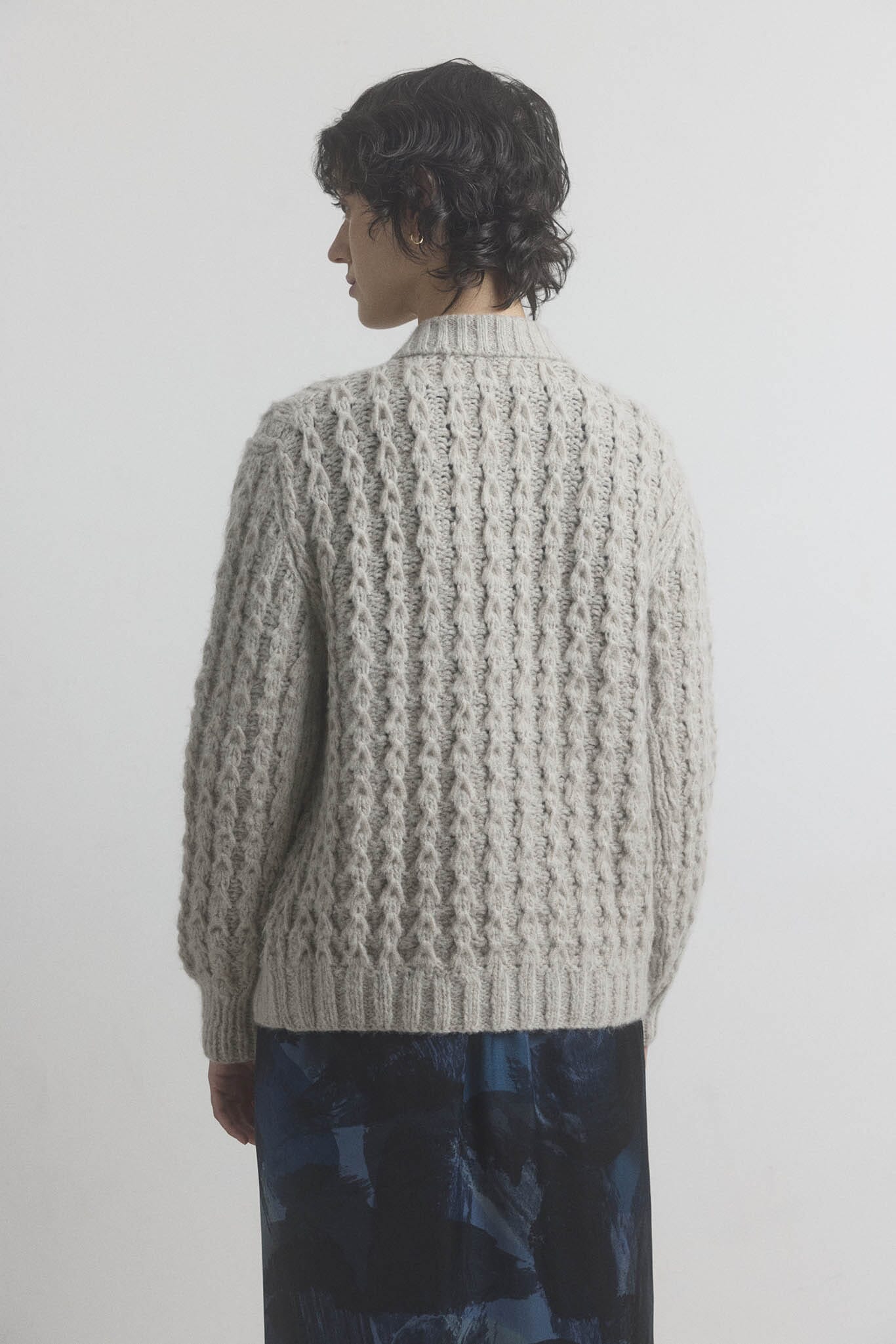A woman facing the back wearing a textured beige sweater against a plain background