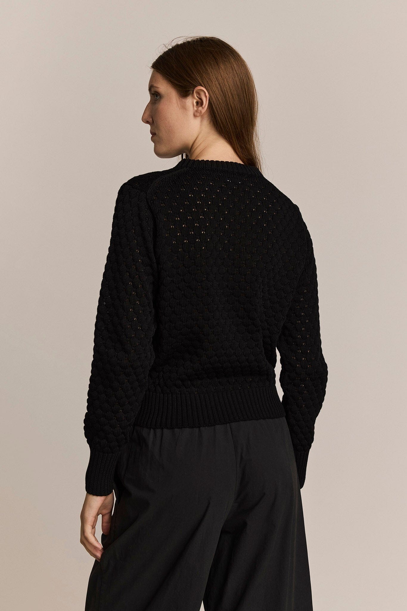 Woman wearing a black textured sweater against a beige background