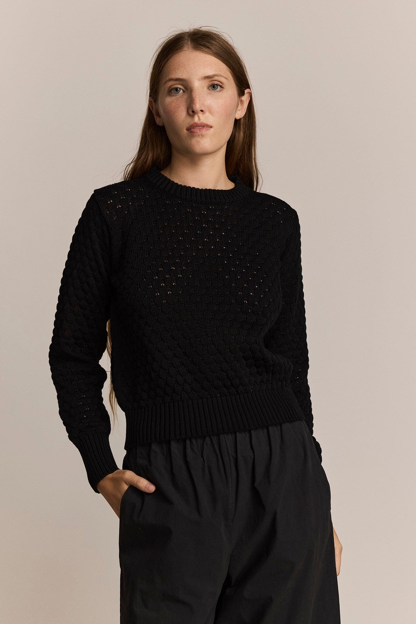 Woman wearing a black textured sweater and black pants against a beige background