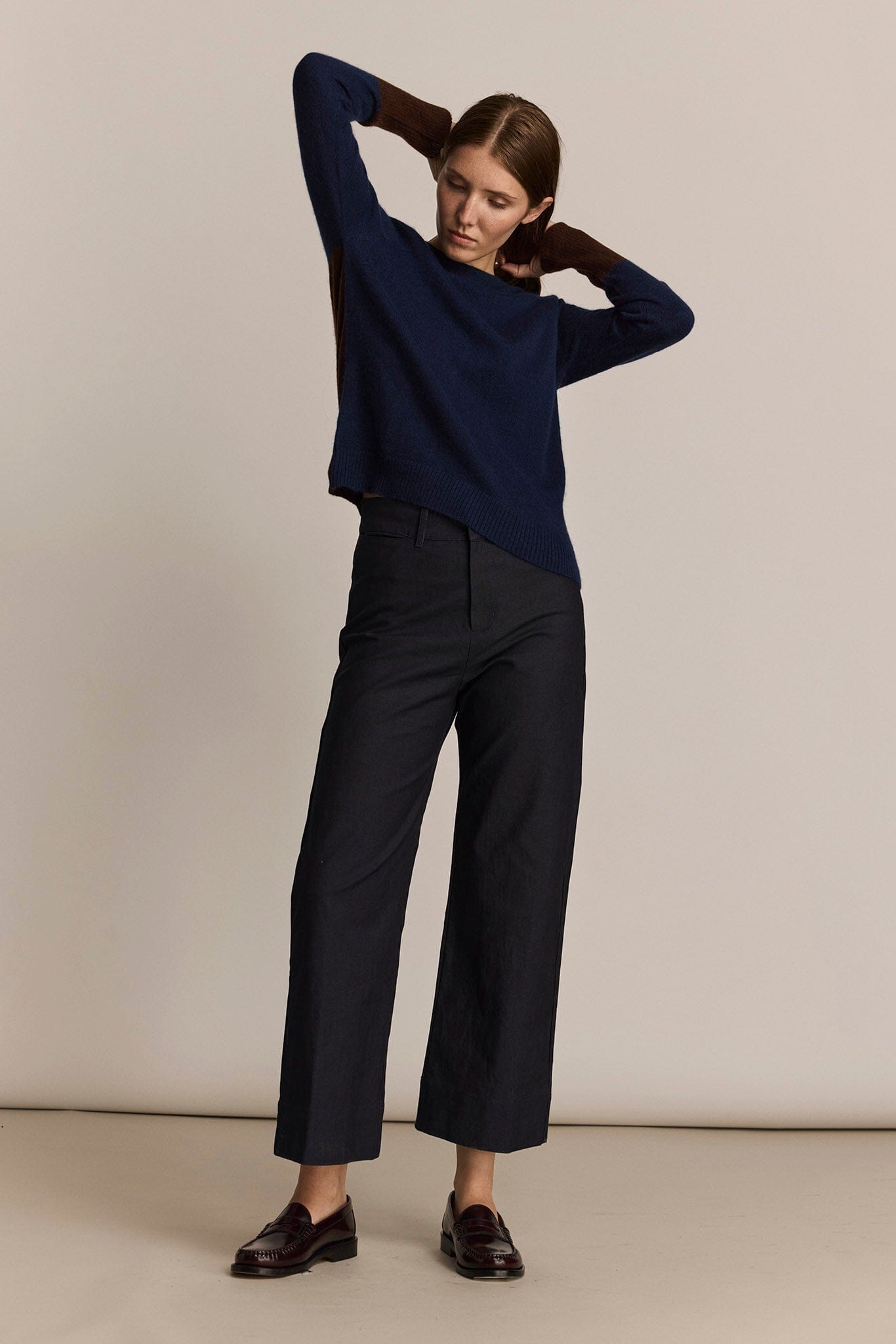 Woman wearing a navy sweater and black straight leg pants against a beige background