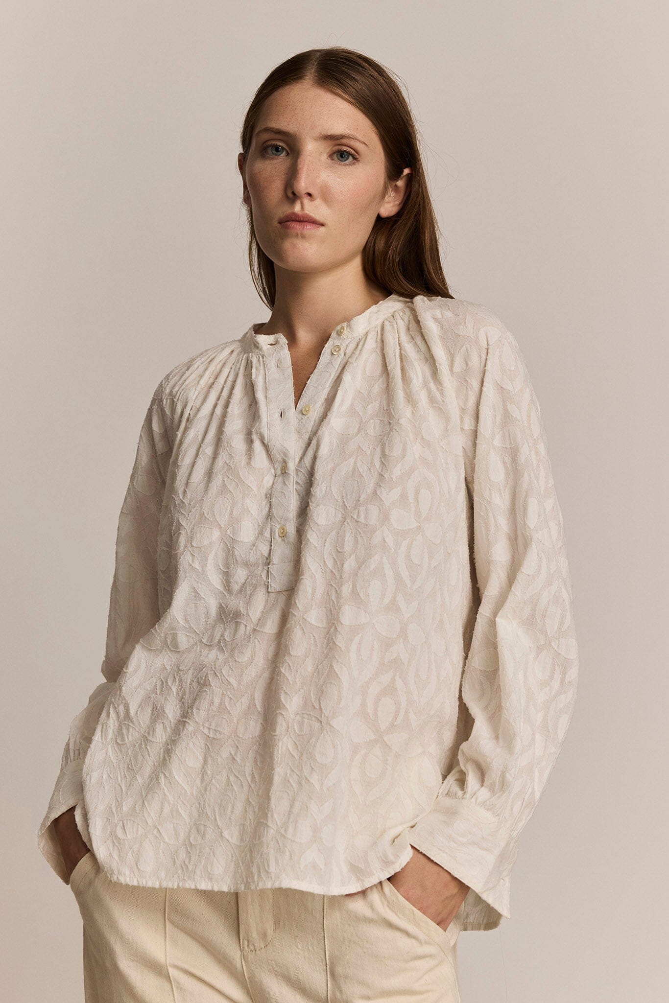 Woman wearing a textured floral patterned shirt against a plain background