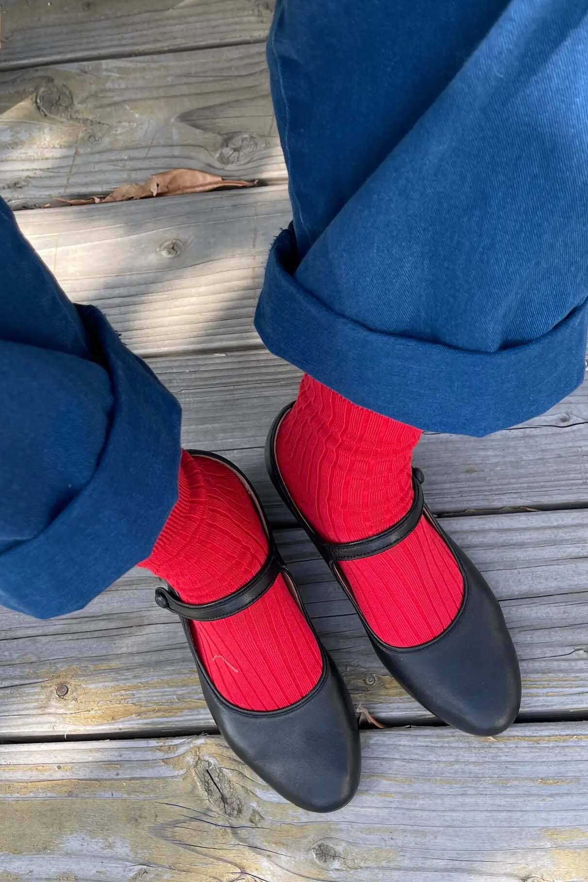 Black mary jane shoes with red ribbed socks worn on a wooden floor