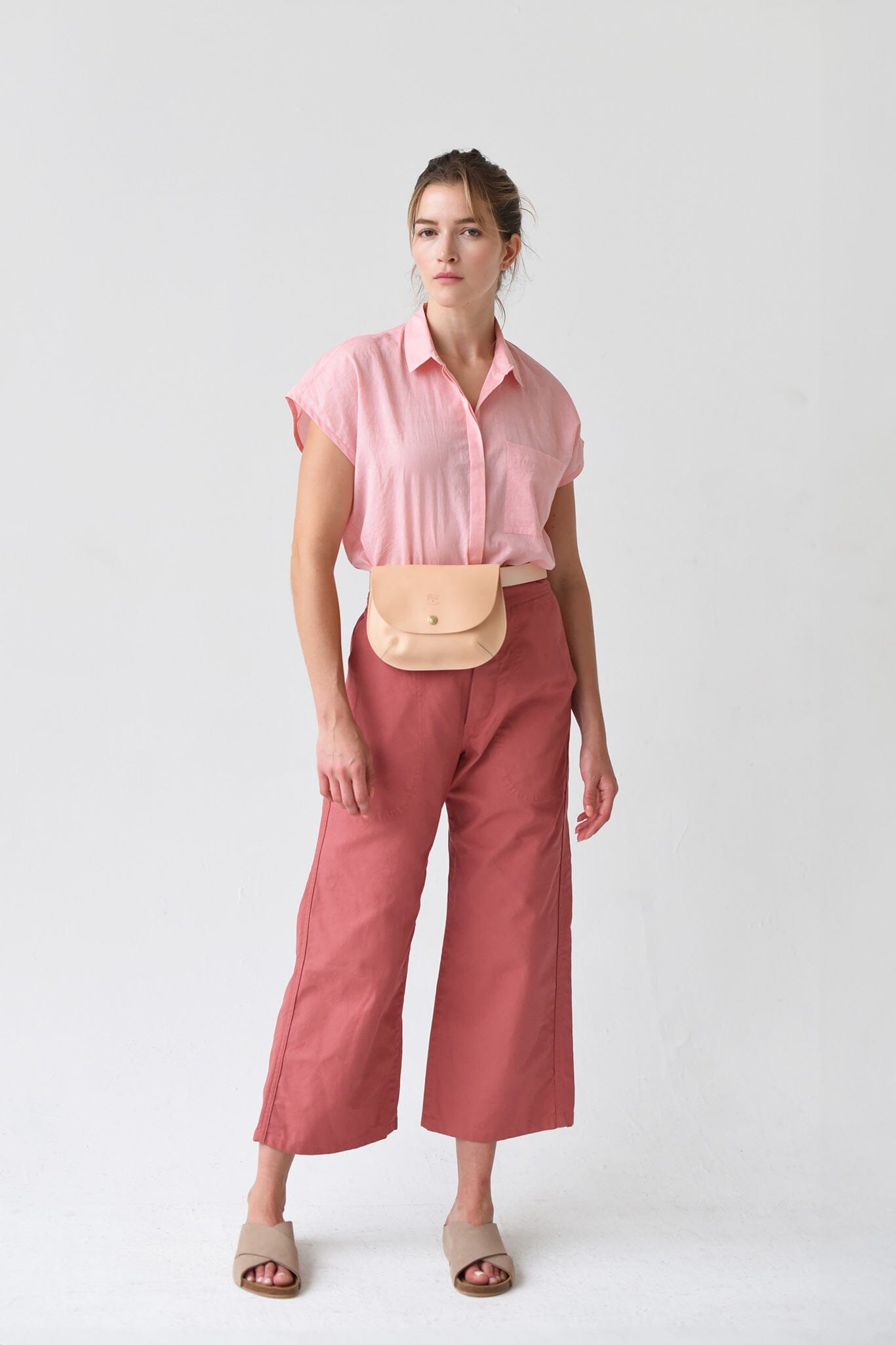 A woman wears a pink short sleeve top with a beige crossbody leather bag.