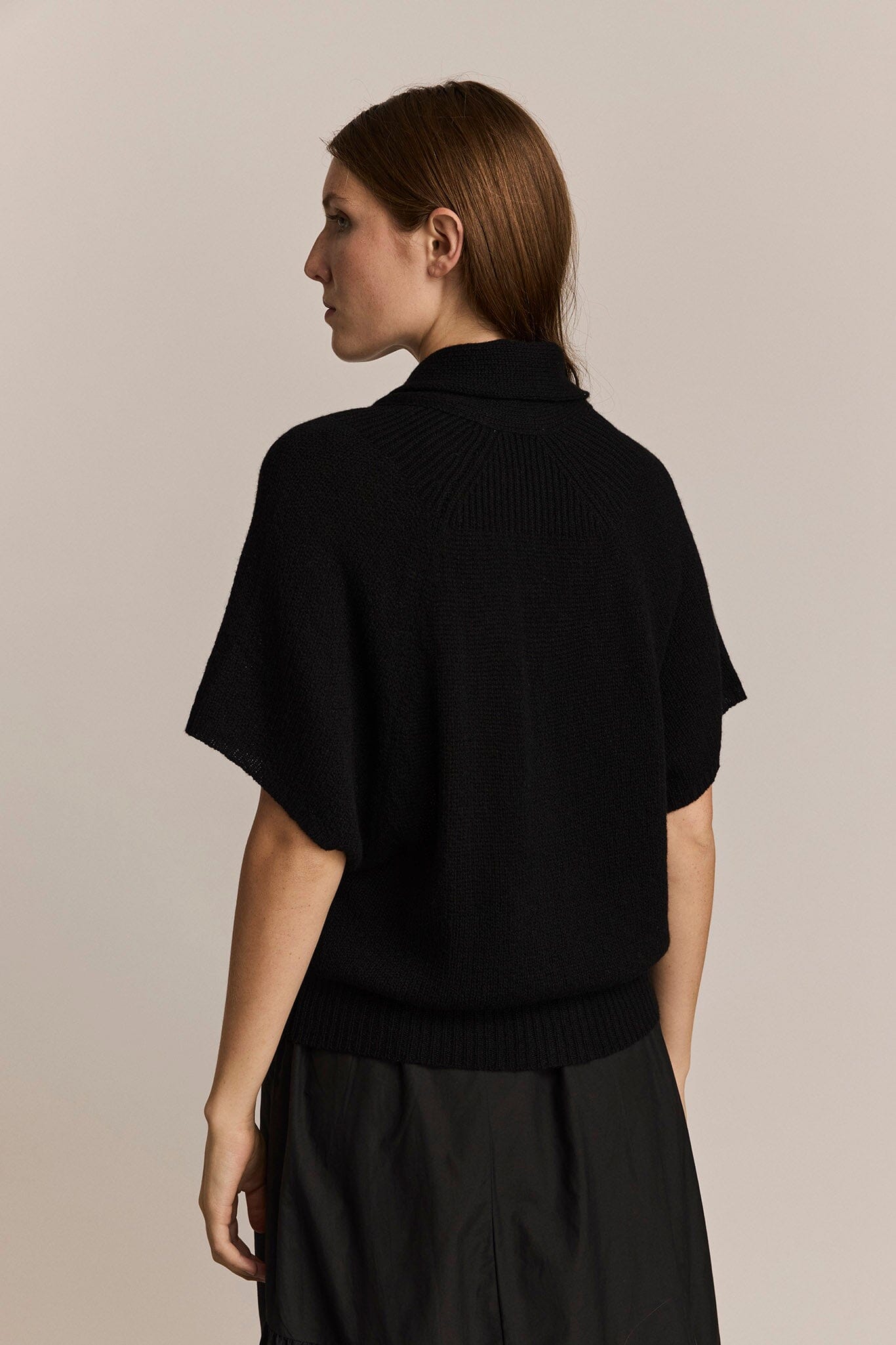 Woman wearing a black cashmere short sleeve sweater against a beige background
