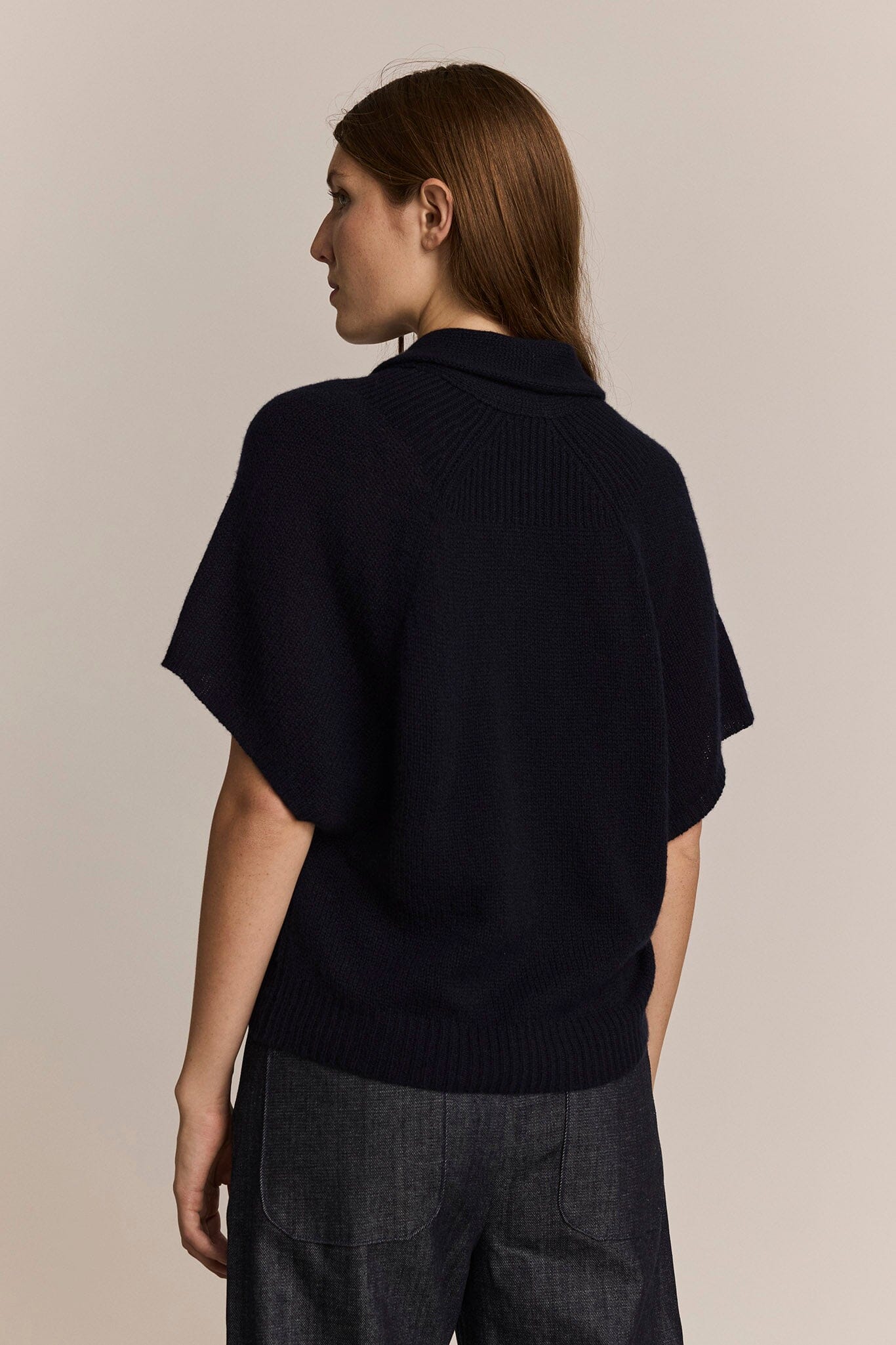 Person wearing a navy short sleeve cashmere sweater on a beige background