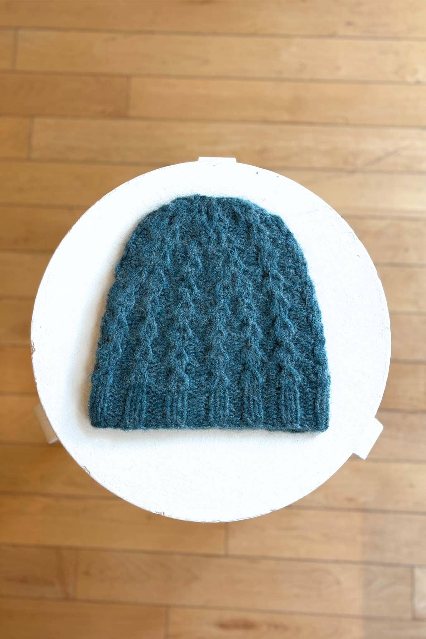 Green blue knitted beanie on a white circular object against a wooden floor background