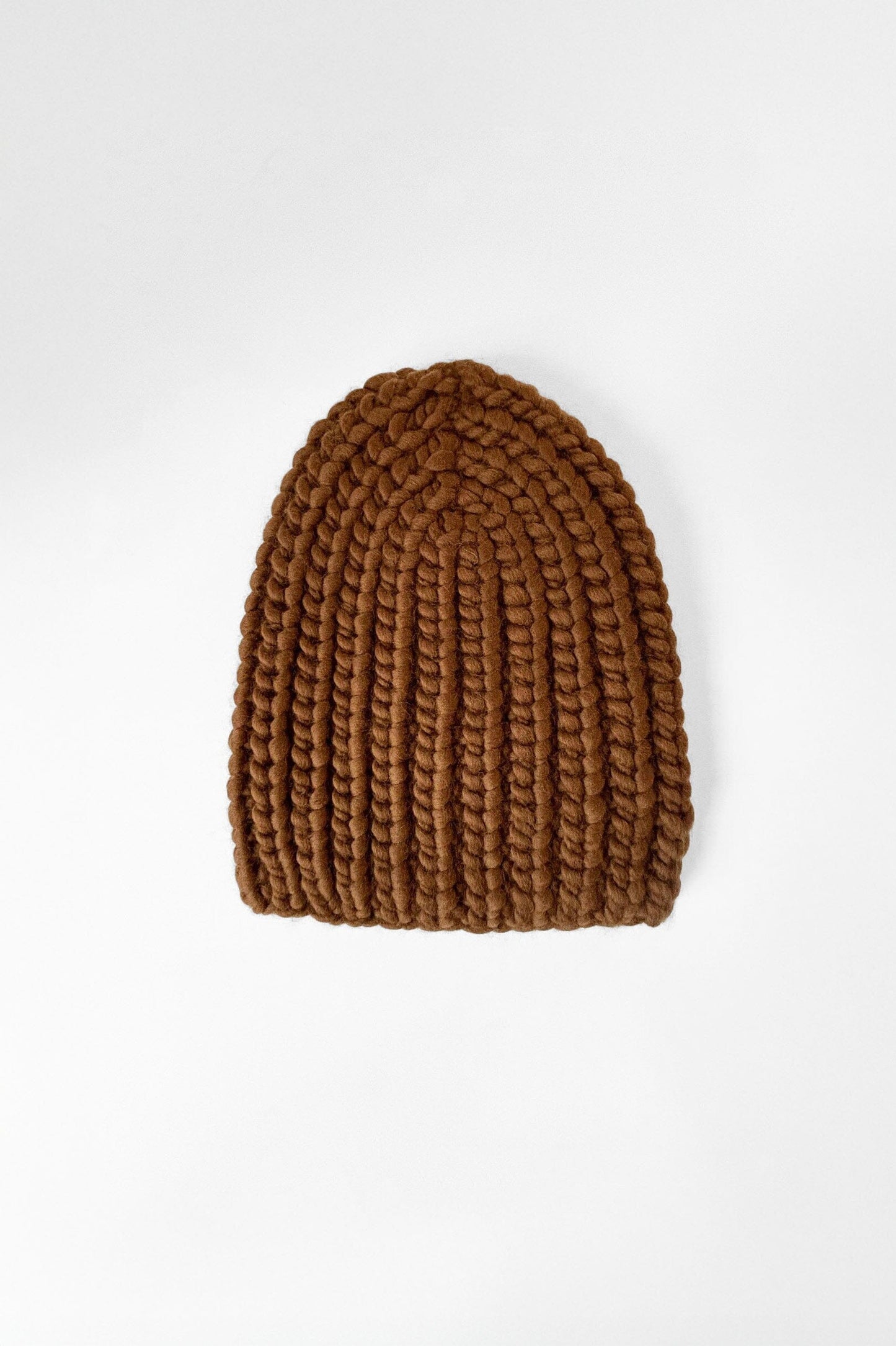 A caramel brown, chunky knit beanie hat on a plain background.