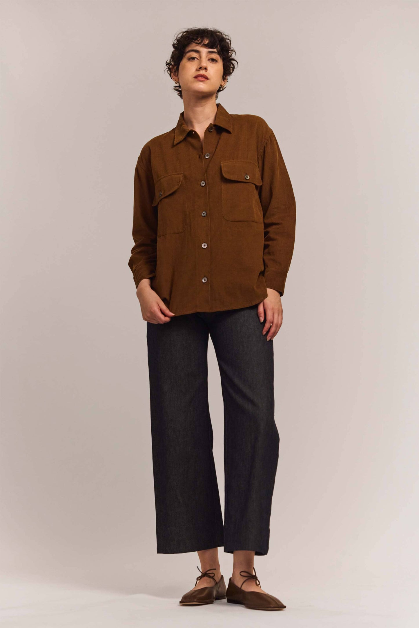 Person wearing a brown jacket and dark pants on a white background