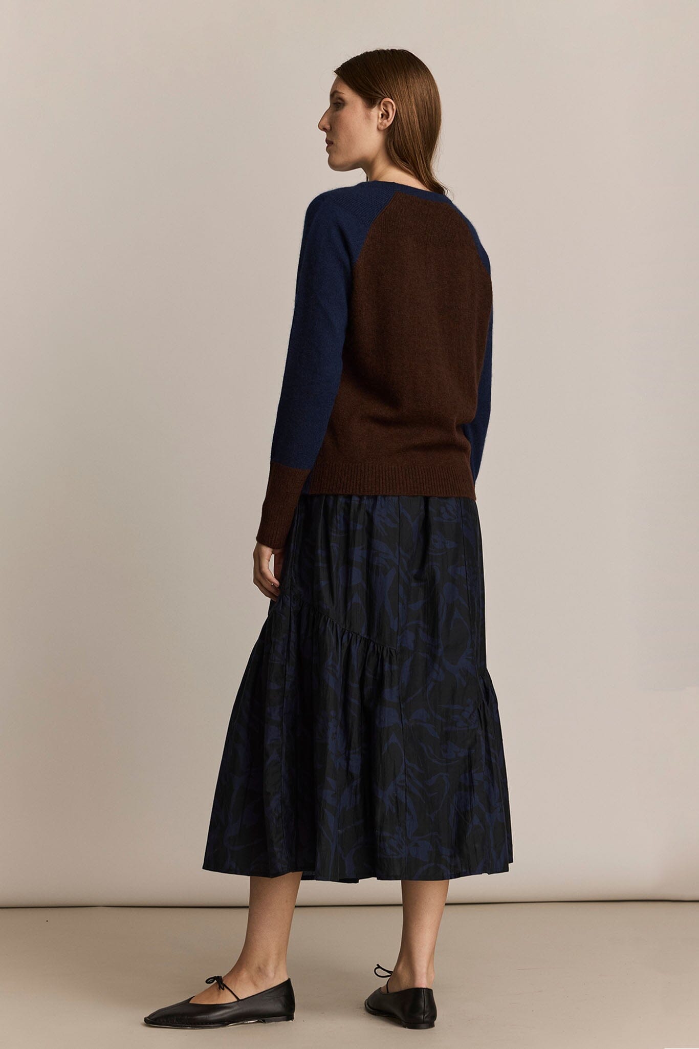 Woman wearing a brown sweater and dark blue patterned skirt on a beige background