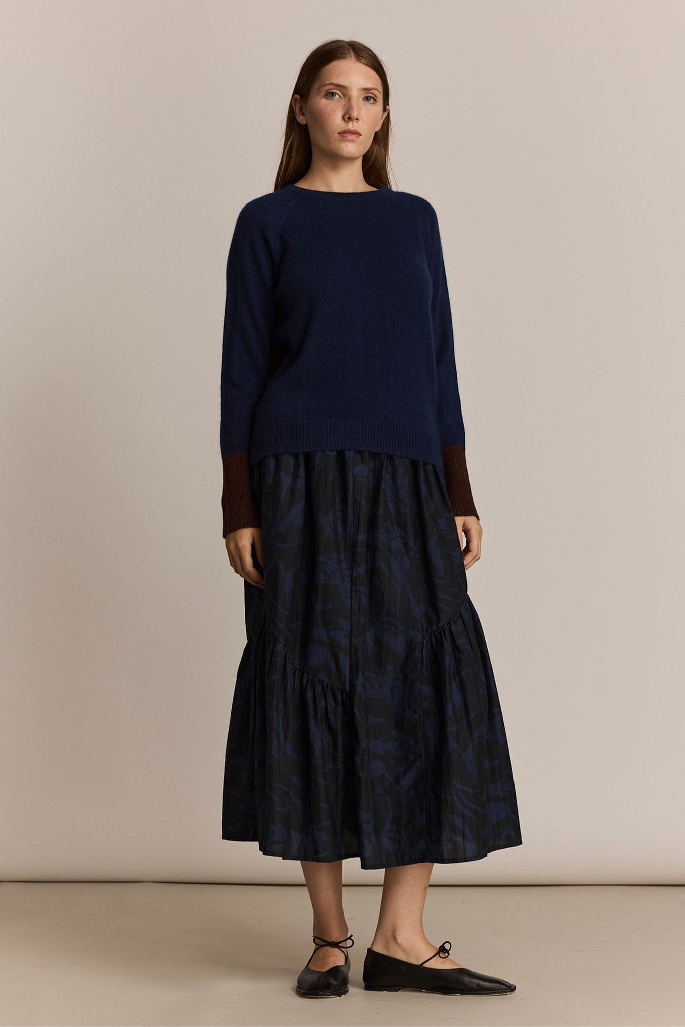 Woman wearing a navy blue sweater and patterned navy skirt against a beige background