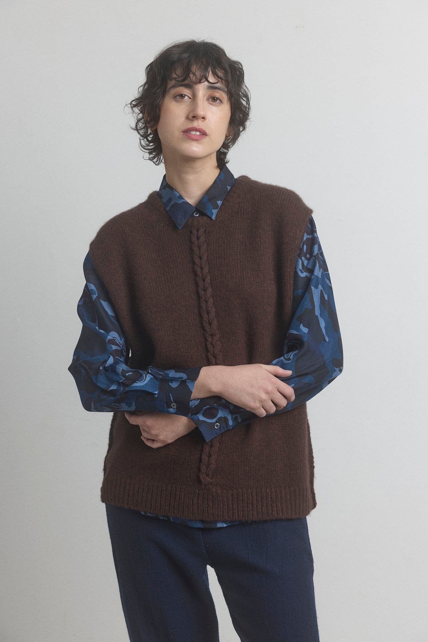 Woman wearing a merino brown sweater vest on a plain background.