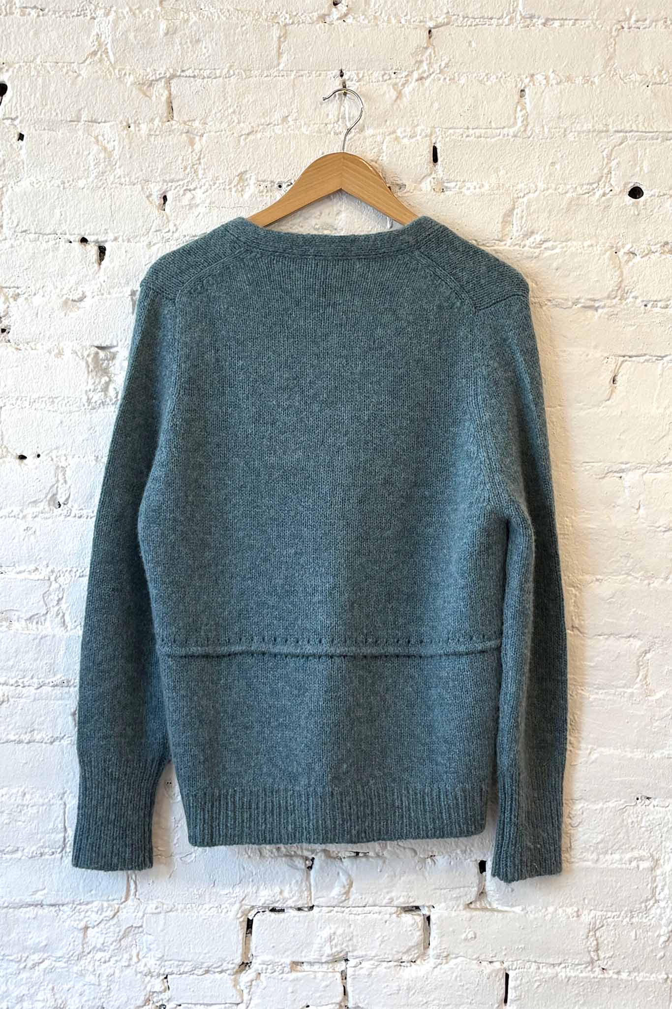 Green sweater on a wooden hanger against a white brick wall