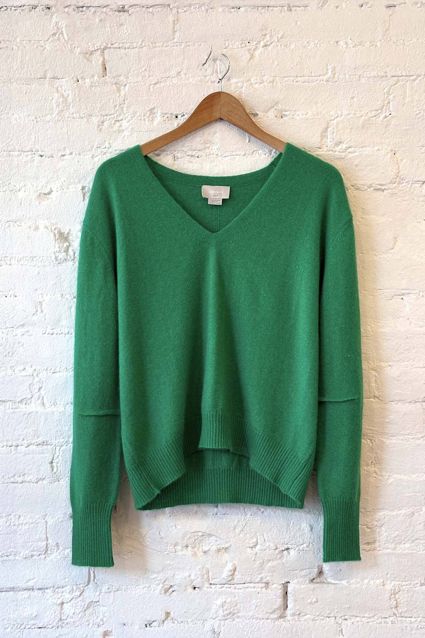Green v-neck sweater on a wooden hanger against a white brick wall