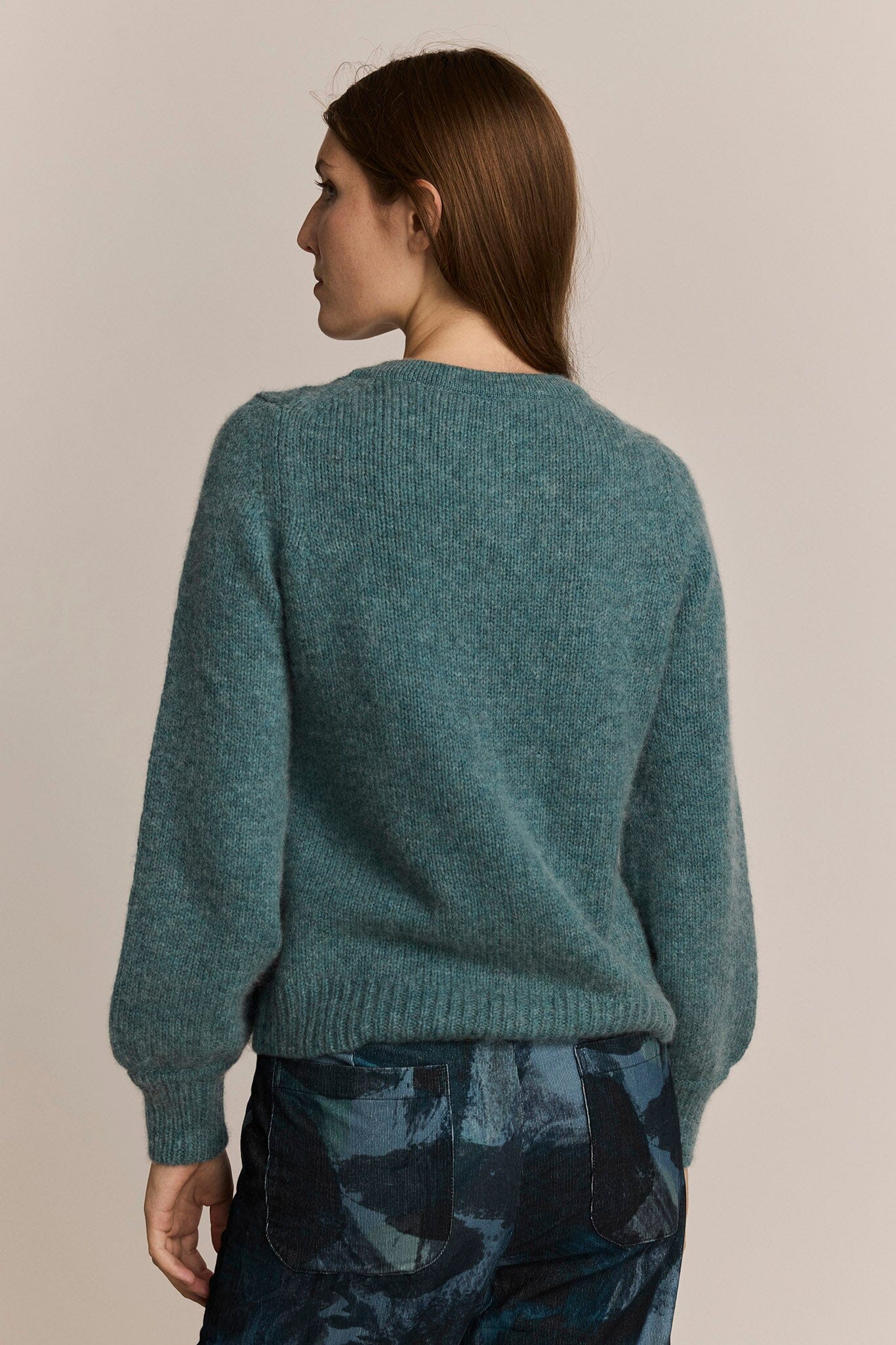 Person wearing a teal sweater with a neutral background