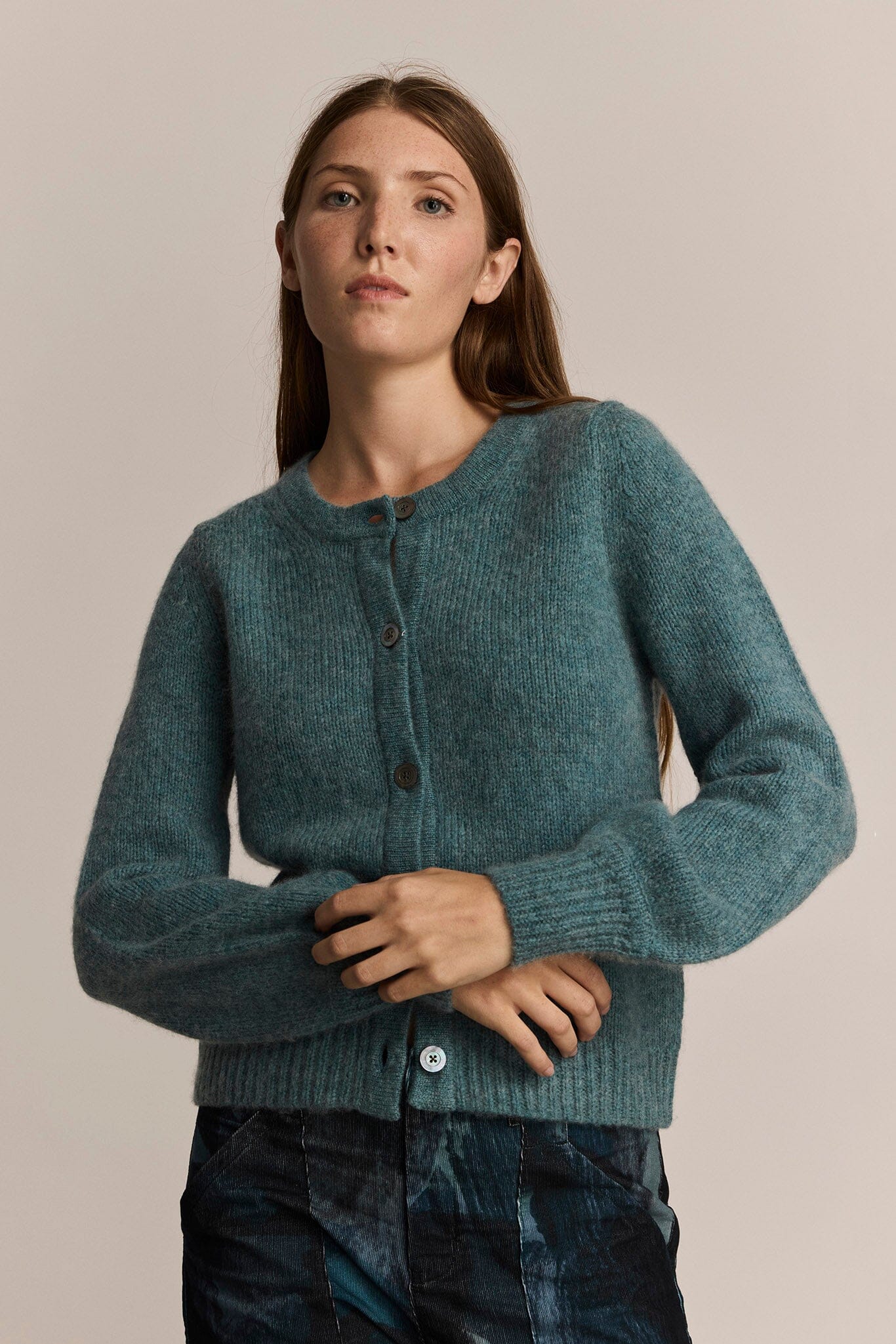 Woman wearing a teal knitted cardigan against a plain background