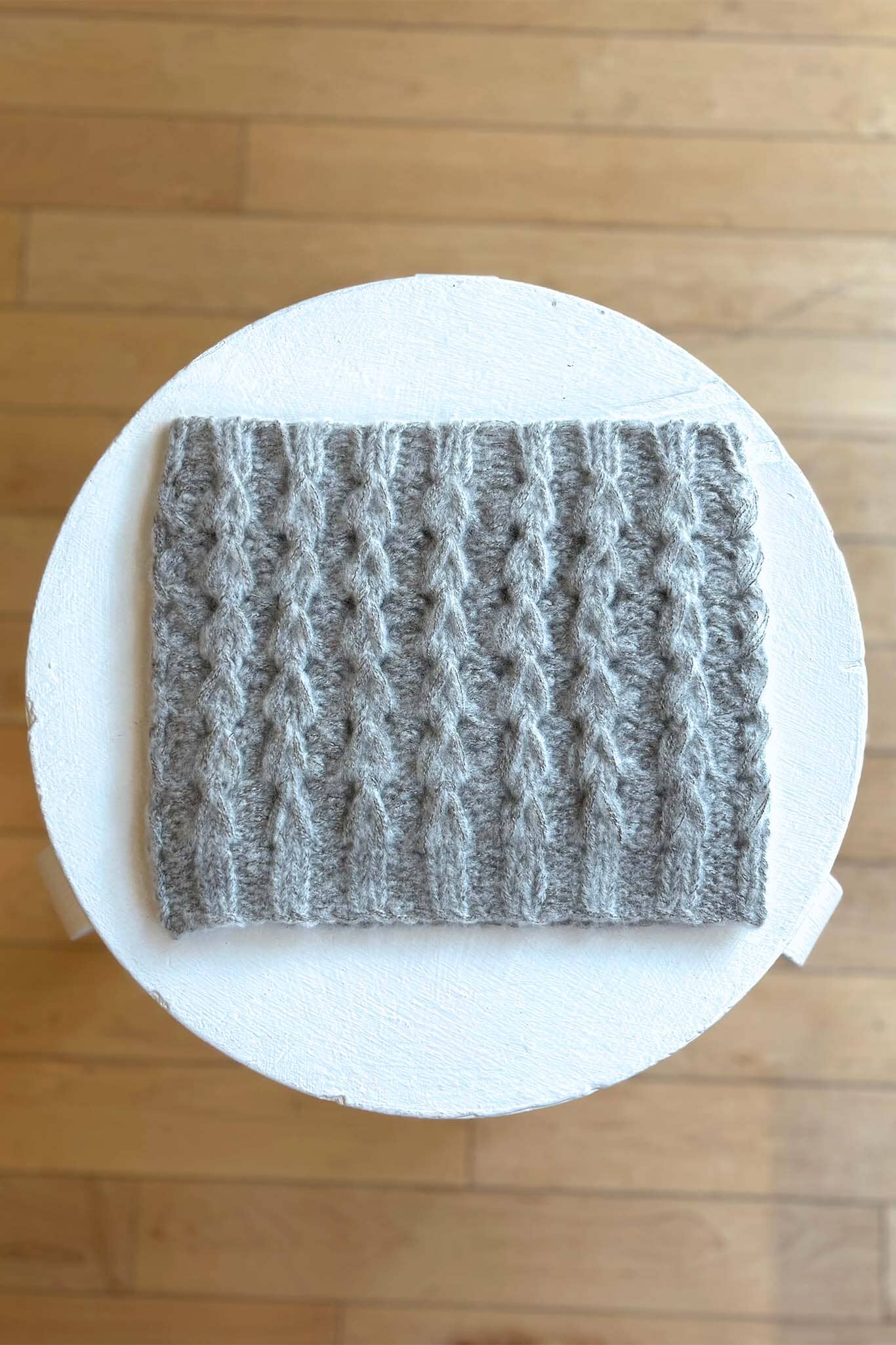 Gray textured square funnelneck on a white circular platform with a wooden floor background