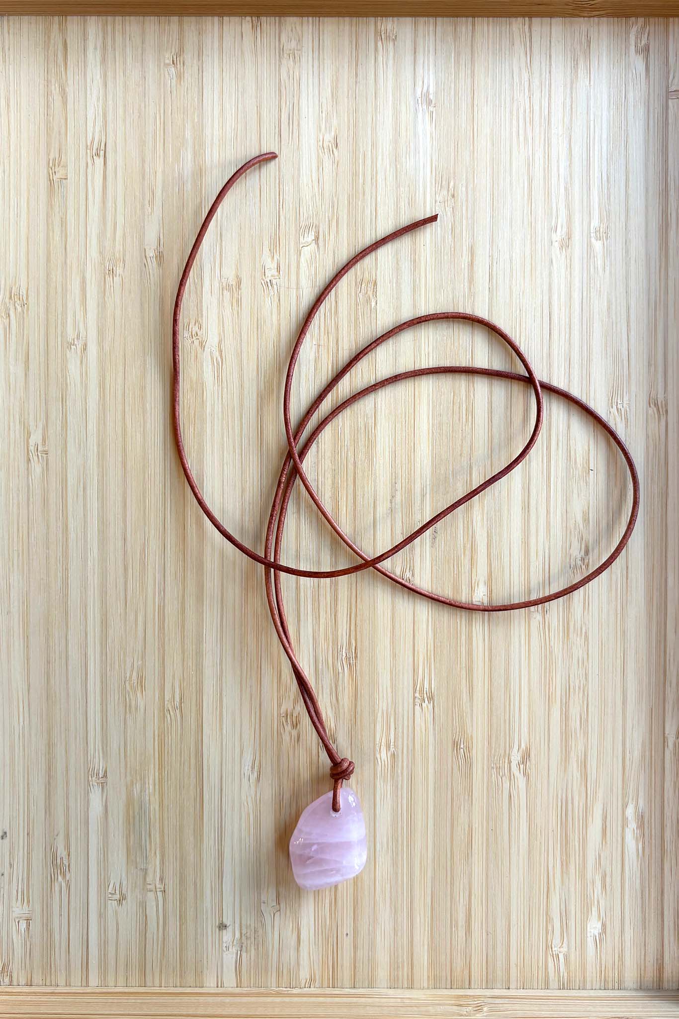 Brown cord necklace with a round organic pink stone pendent on a wooden surface