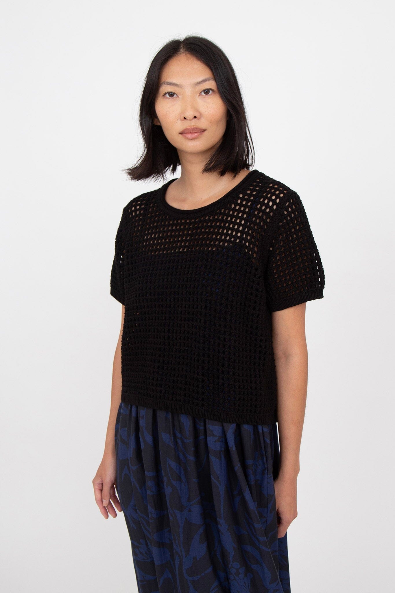 A person wearing a black short sleeve mesh knit tee and a blue patterned skirt.