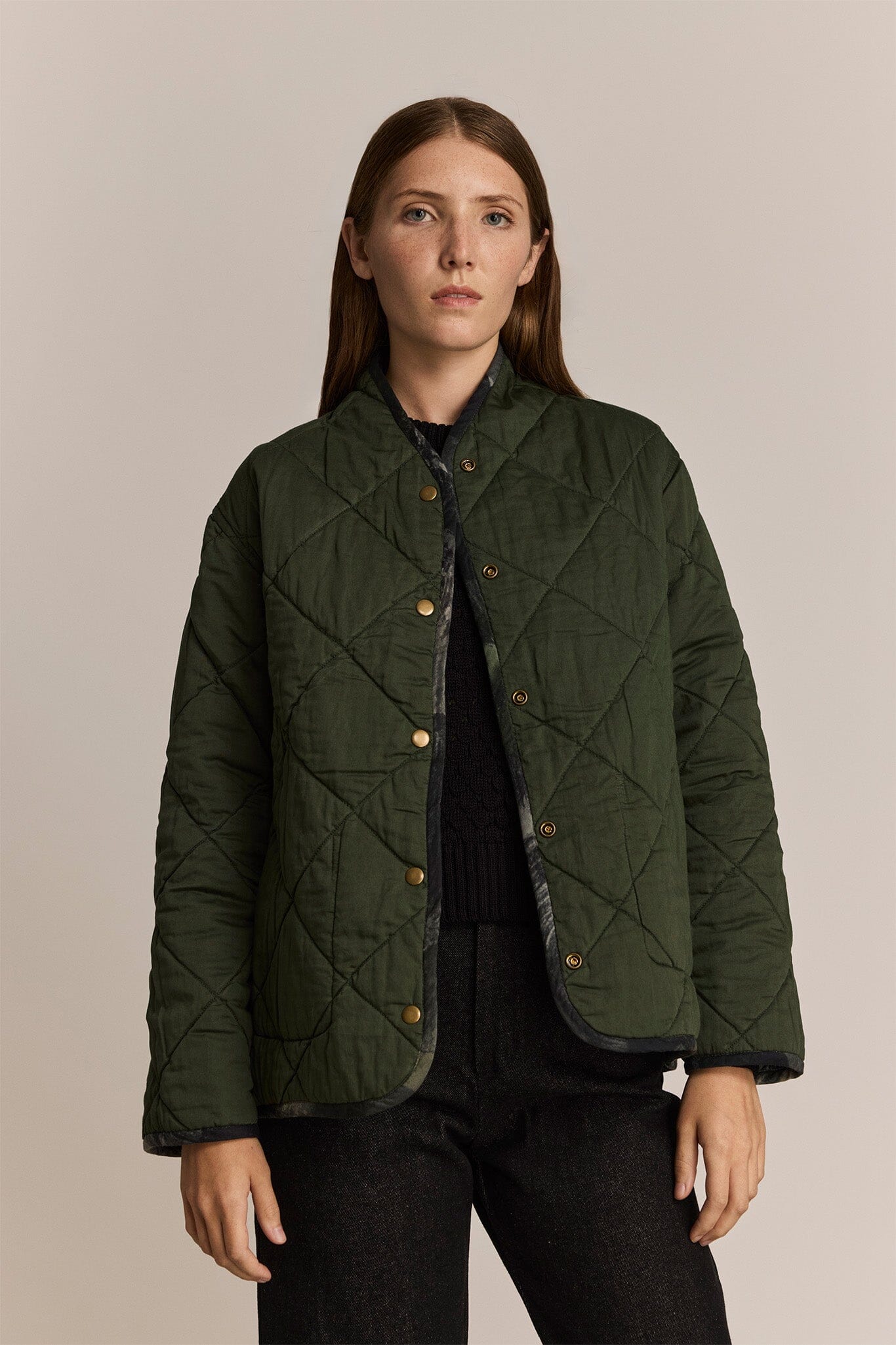 Woman wearing a green quilted jacket against a beige background