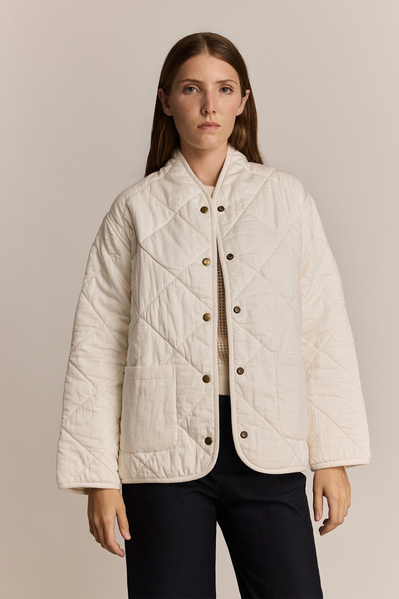 Woman wearing a cream quilted jacket against a beige background