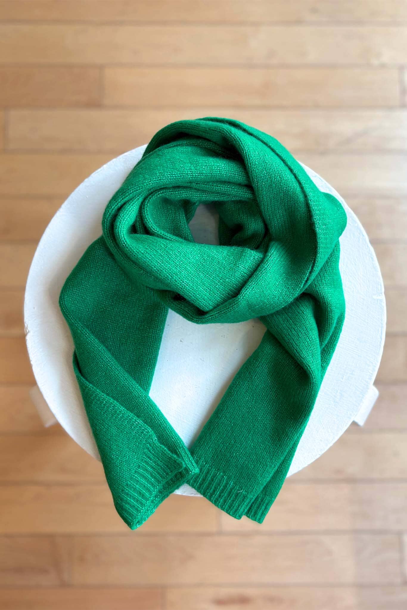 Green cashmere scarf on a white plate with a wooden surface background