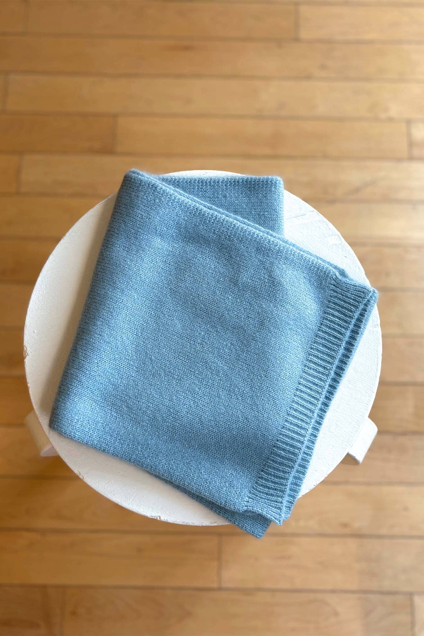 Blue soft knitted scarf on a white plate with a wooden floor background