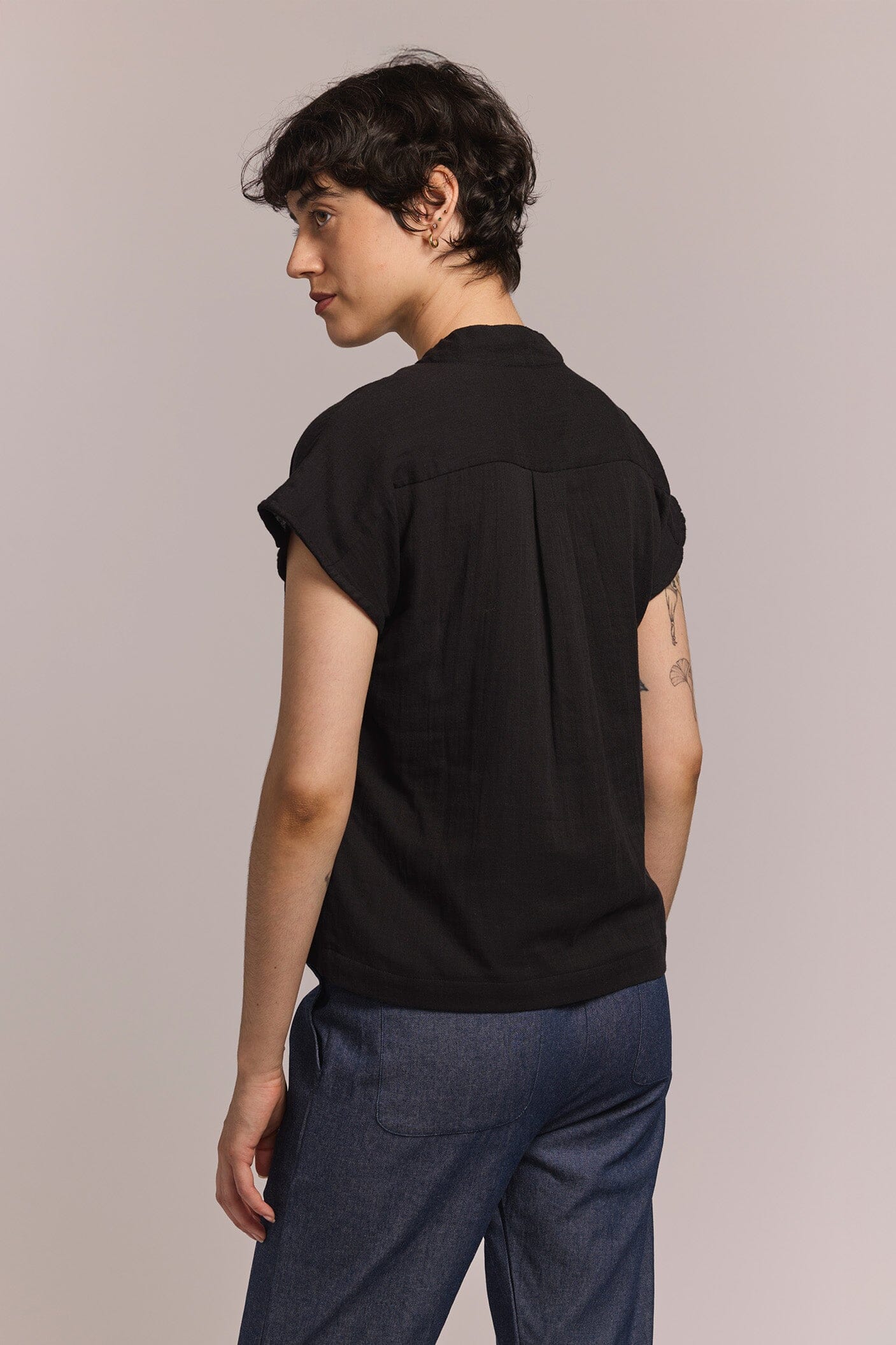 Person wearing a black short-sleeve shirt and blue pants against a beige background