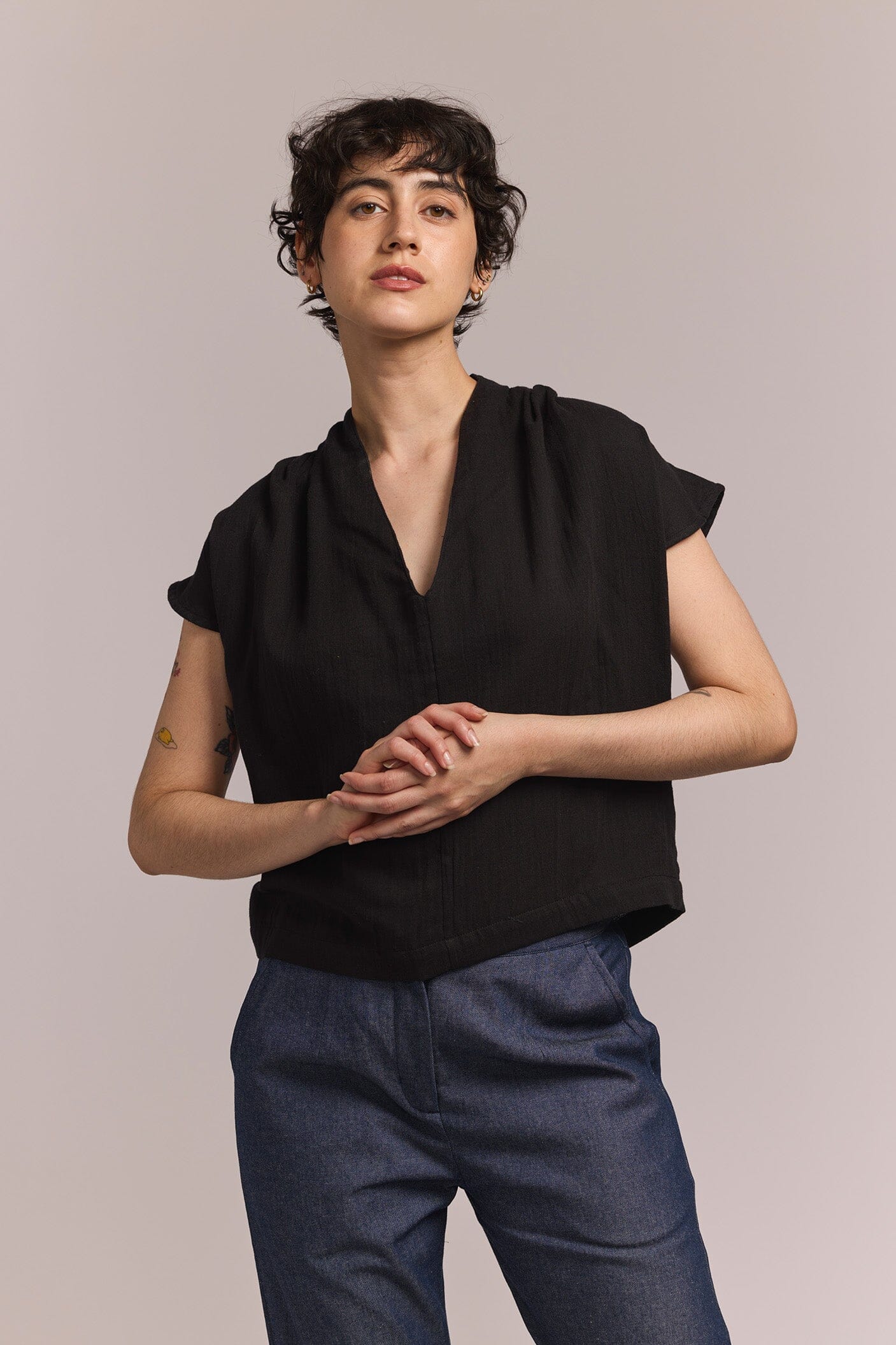 Person wearing a black short sleeve top and blue pants against a plain background