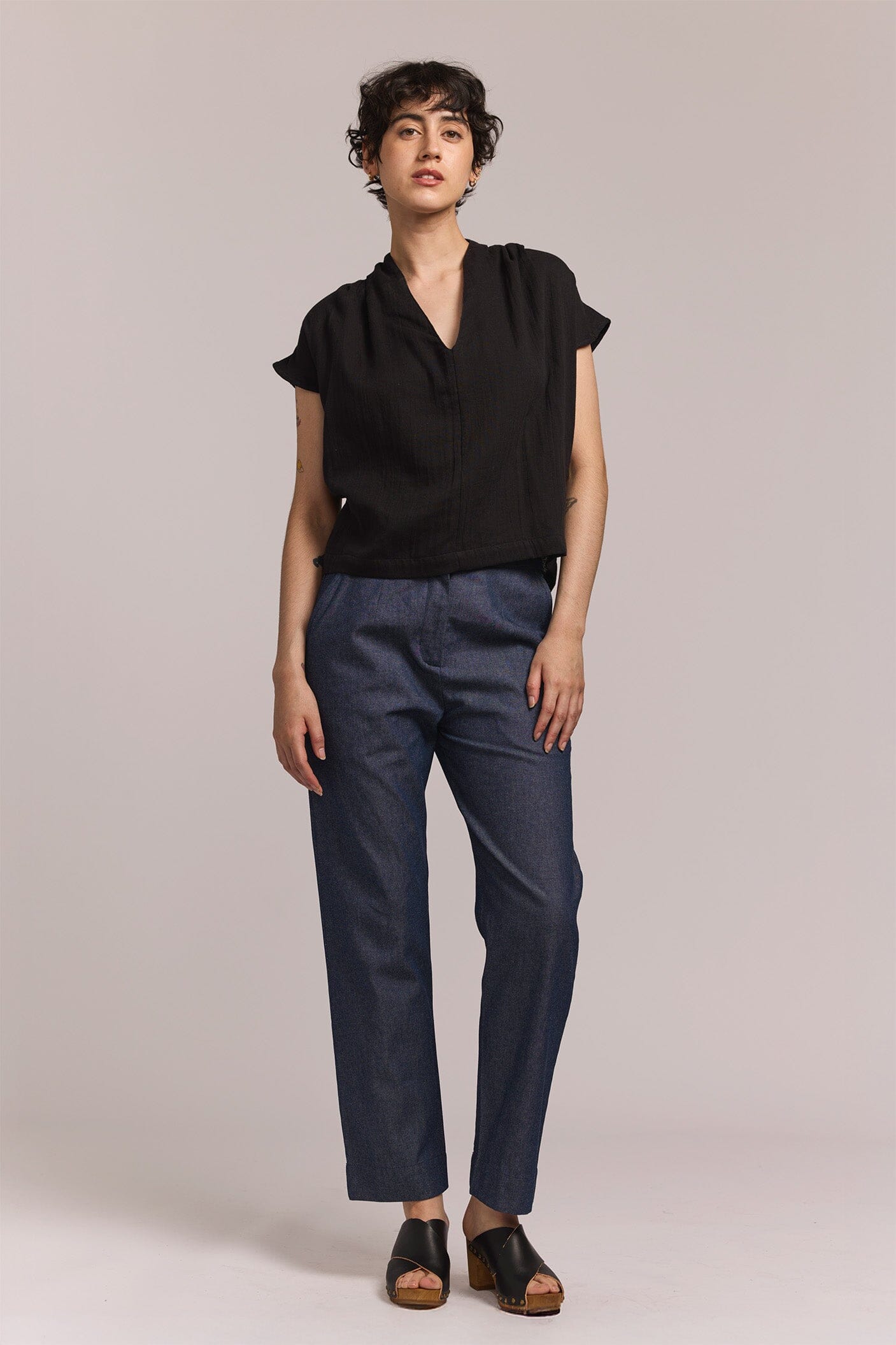 Woman wearing a black short sleeve v-neck top and dark pants on a plain background