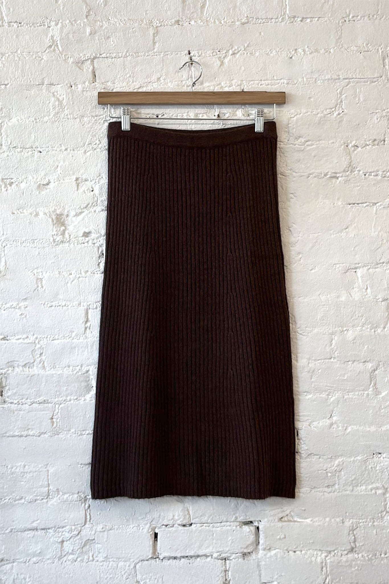 Brown ribbed knit skirt hanging against a white brick wall