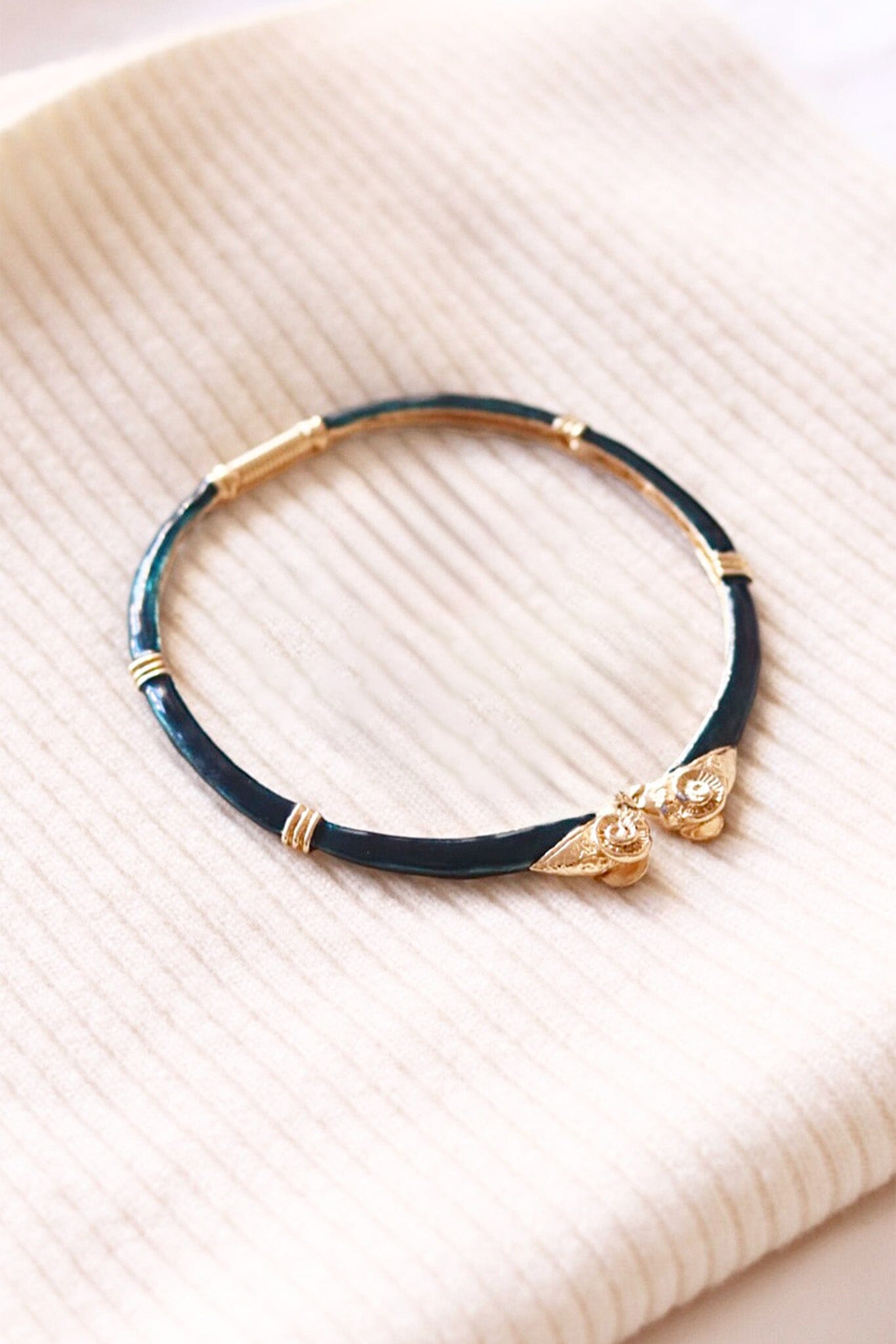 Dark green choker necklace with gold accents and rams heads on a beige textured background