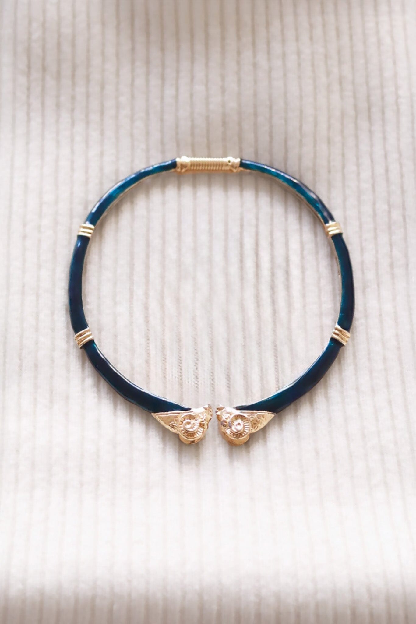 Dark green choker necklace with gold accents and rams heads on a beige textured background