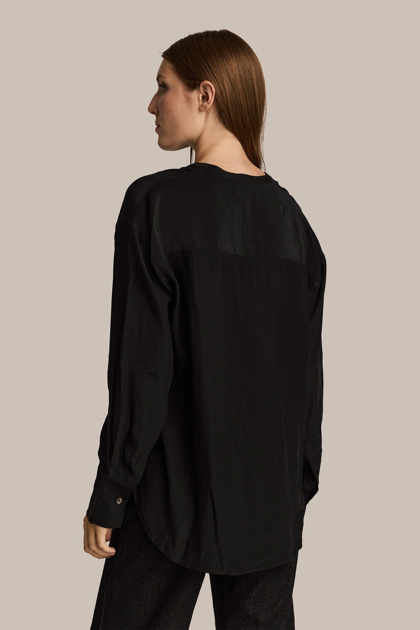 Person wearing a black long sleeve silk shirt against a beige background