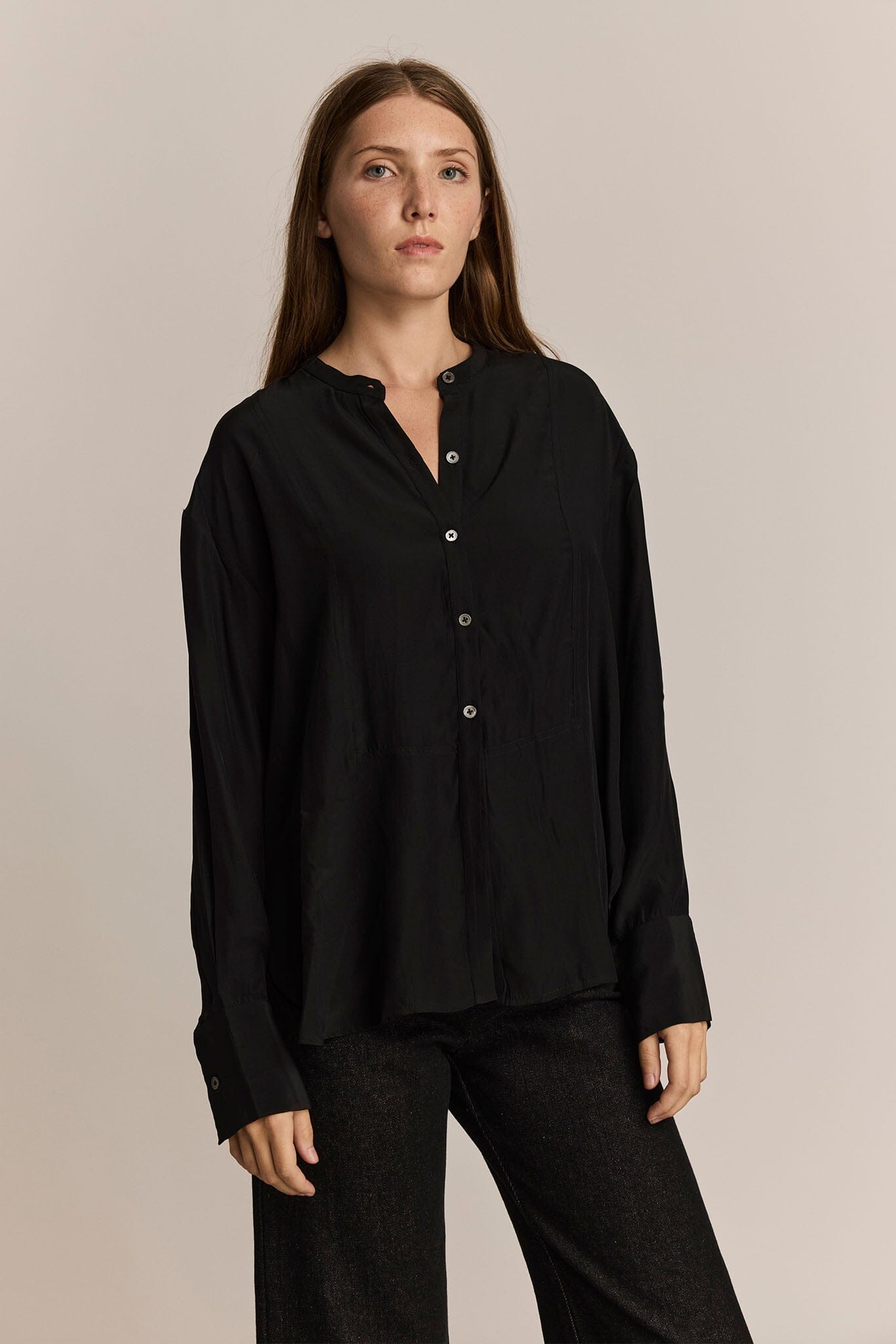 Woman wearing a black long sleeve button-up shirt and pants against a beige background