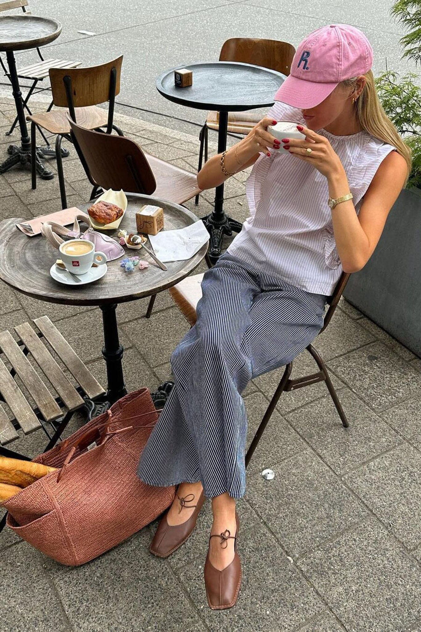Woman sitting at an outdoor cafe table, wearing a pink cap and white shirt and Alohas brown sway square toed flat shoes