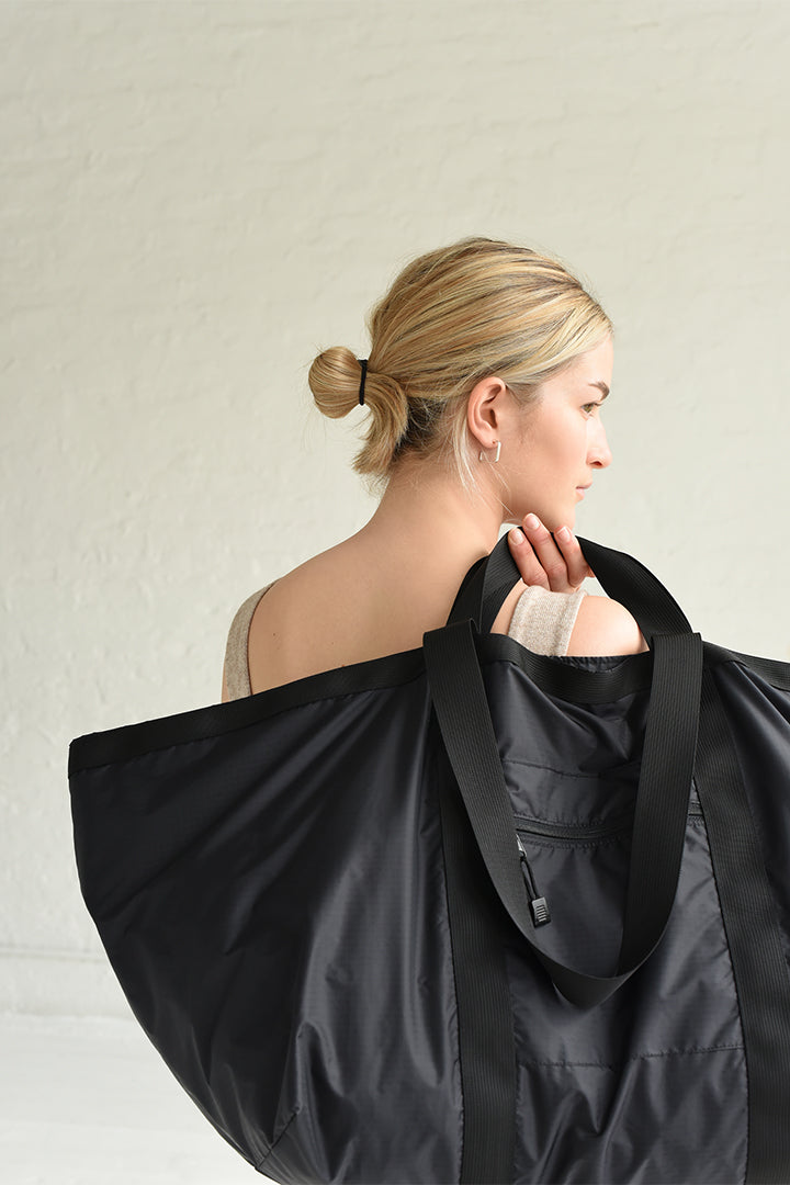 A woman holds the 8.6.4. large black nylon waterproof duffle bag