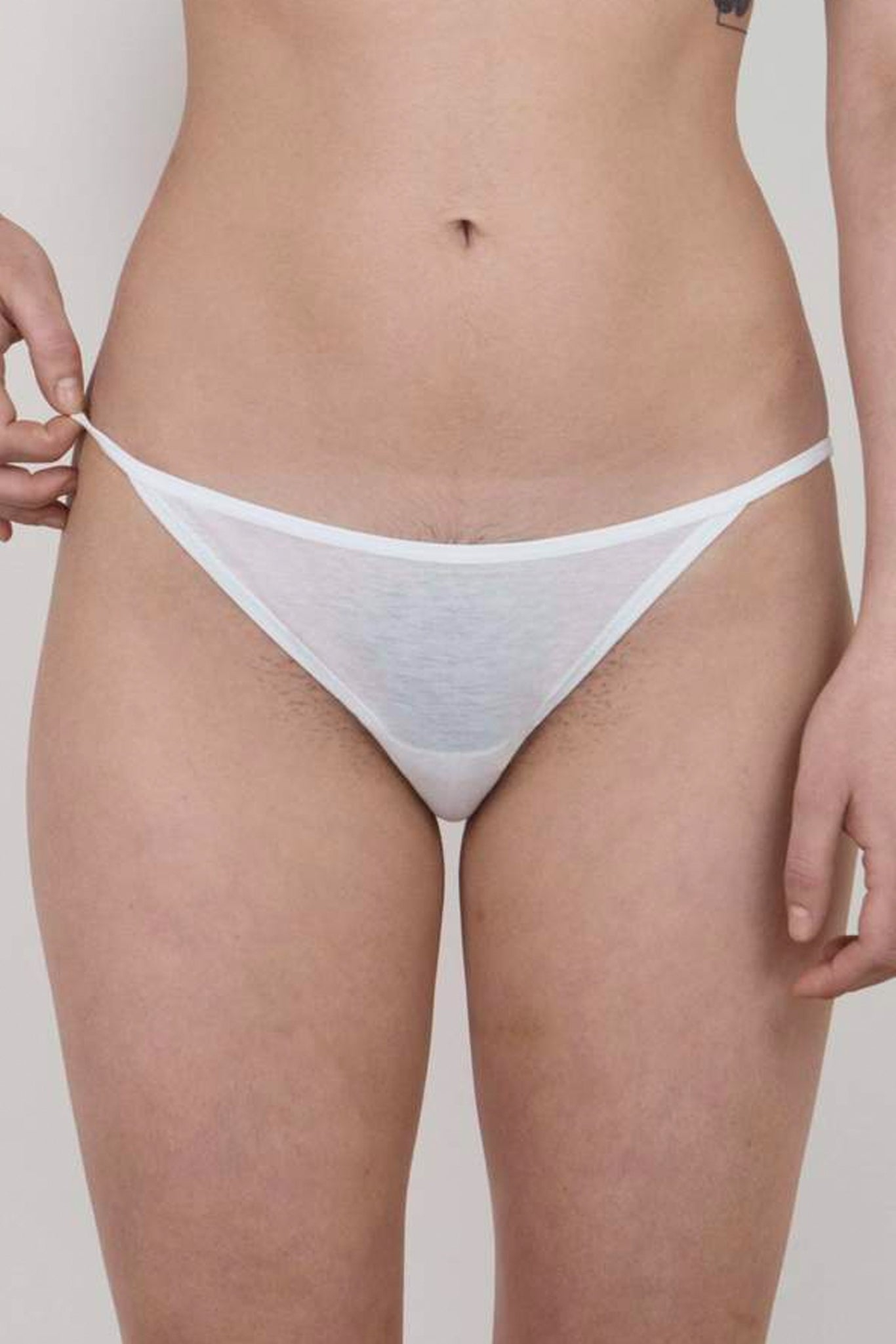 This image features the Oddobody String Bikini in a chalk white color, emphasizing its light and sheer fabric. The bikini is designed with a low-rise fit that enhances its delicate and minimalist appeal.