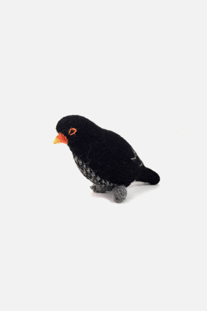 Hand-knit wool black bird bird toy with black body and orange beak, on a white background.