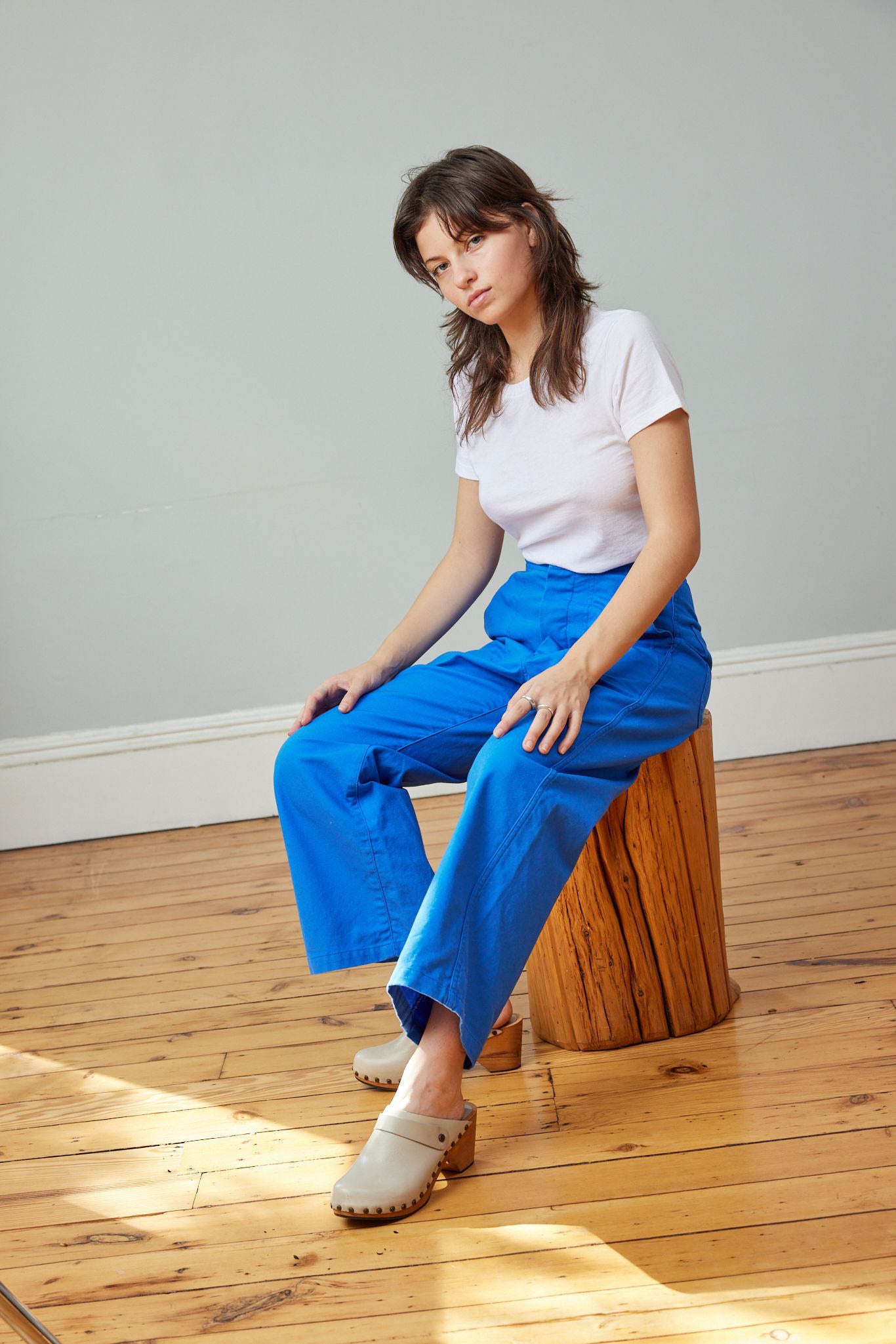 A woman sitting wearing a white t-shirt and cobalt blue high-rise wide-leg crop sailor pant with front pockets.
