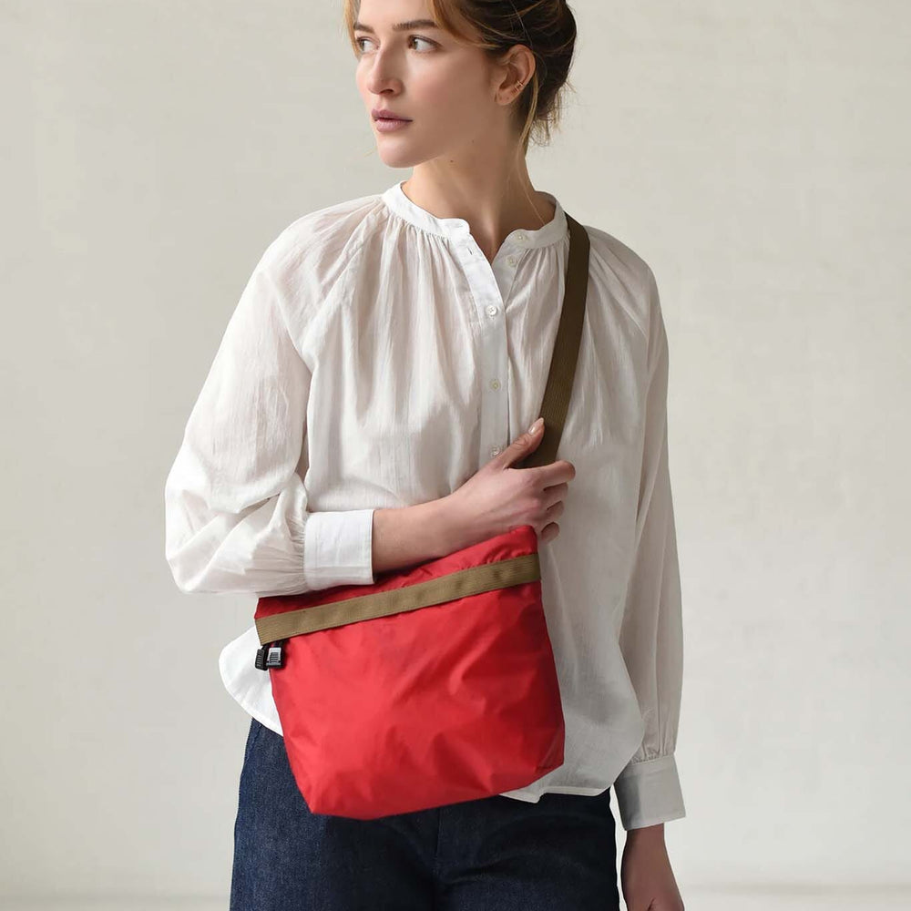 Woman wearing a white blouse and red bag with a brown strap against a plain background