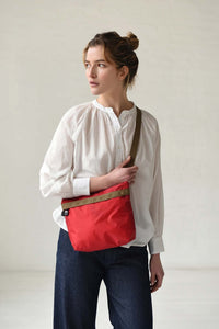 Woman wearing a white blouse and red bag with a brown strap against a plain background