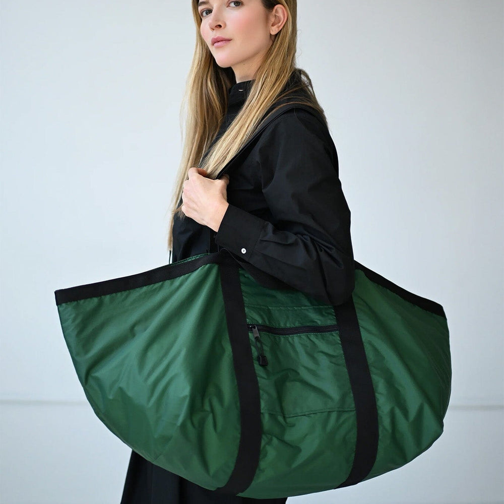 Woman holding a large green nylon duffel bag against a plain background
