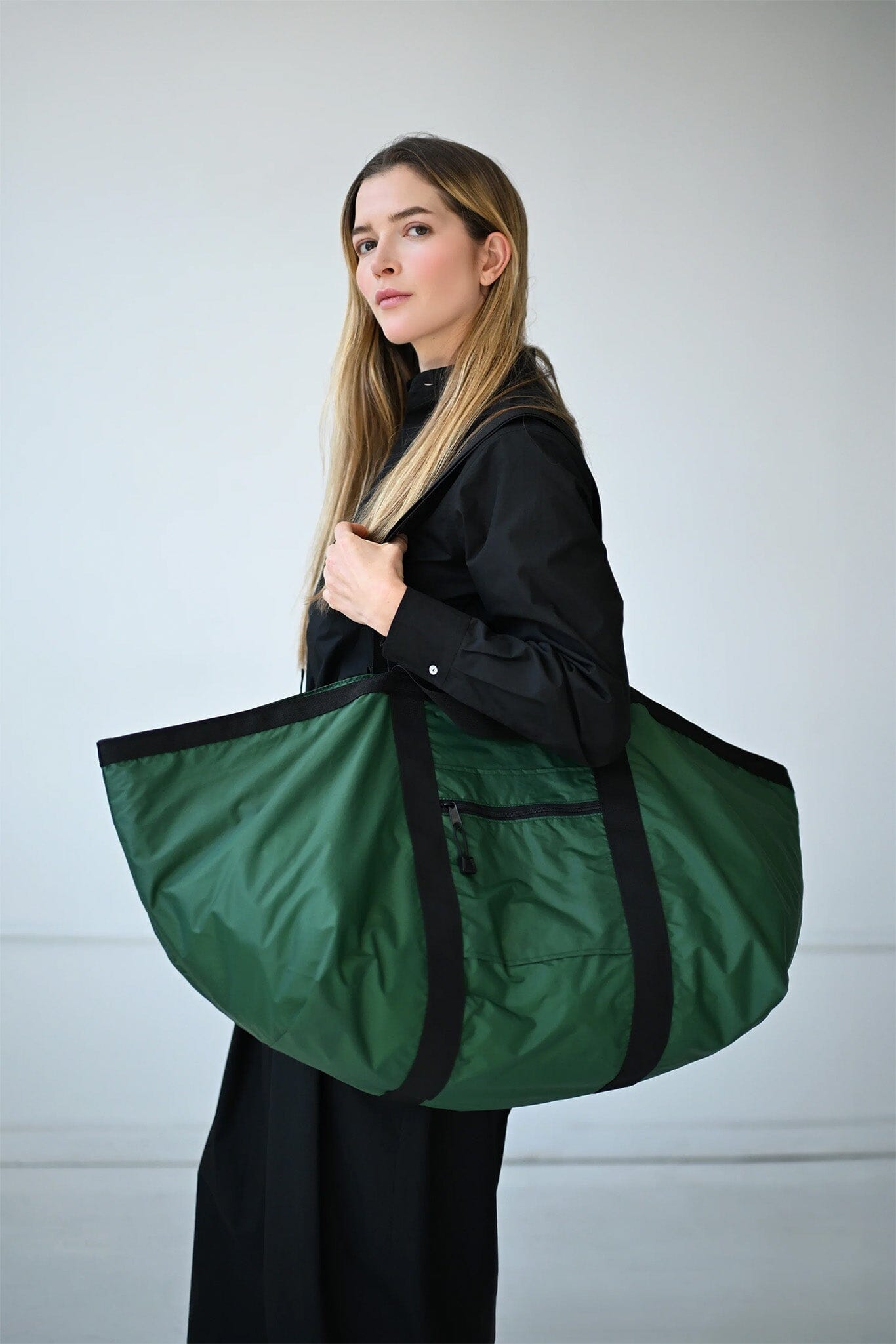 Woman holding a large green nylon duffel bag against a plain background