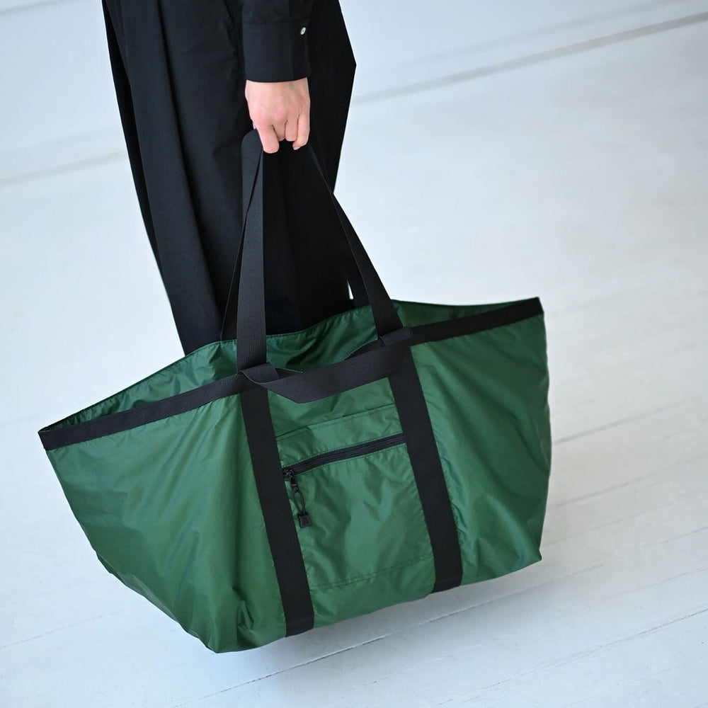 Person holding a green bag with black trim on a white floor.