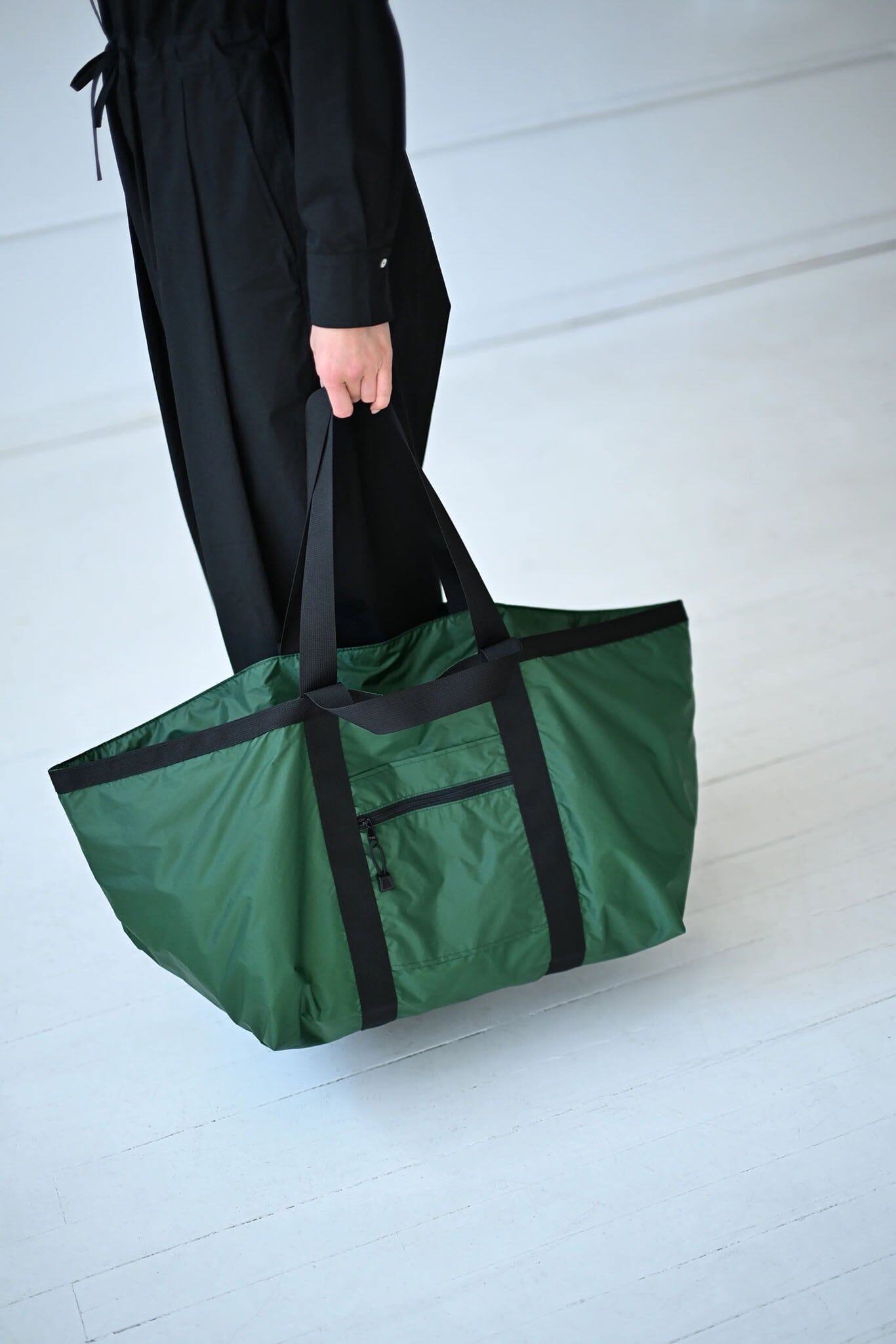 Person holding a green bag with black trim on a white floor.