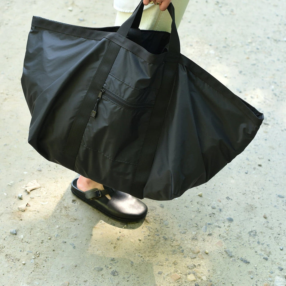 Person holding a large black zipper bag on a concrete surface
