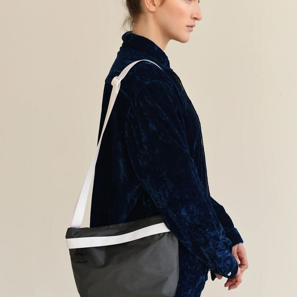 Woman wearing a dark blue jacket with a black and white crossbody bag on a beige background