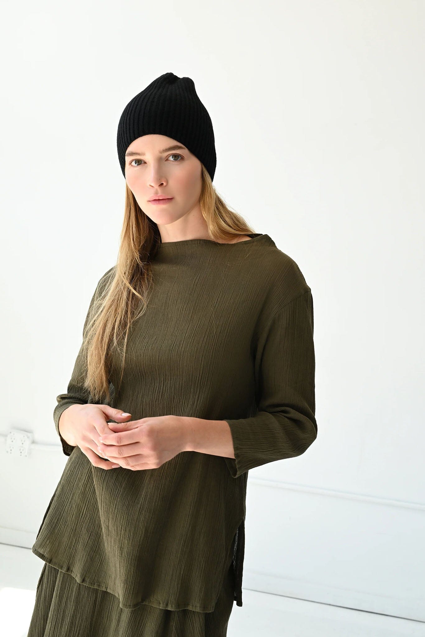 Woman wearing a green blouse and black beanie against a white background
