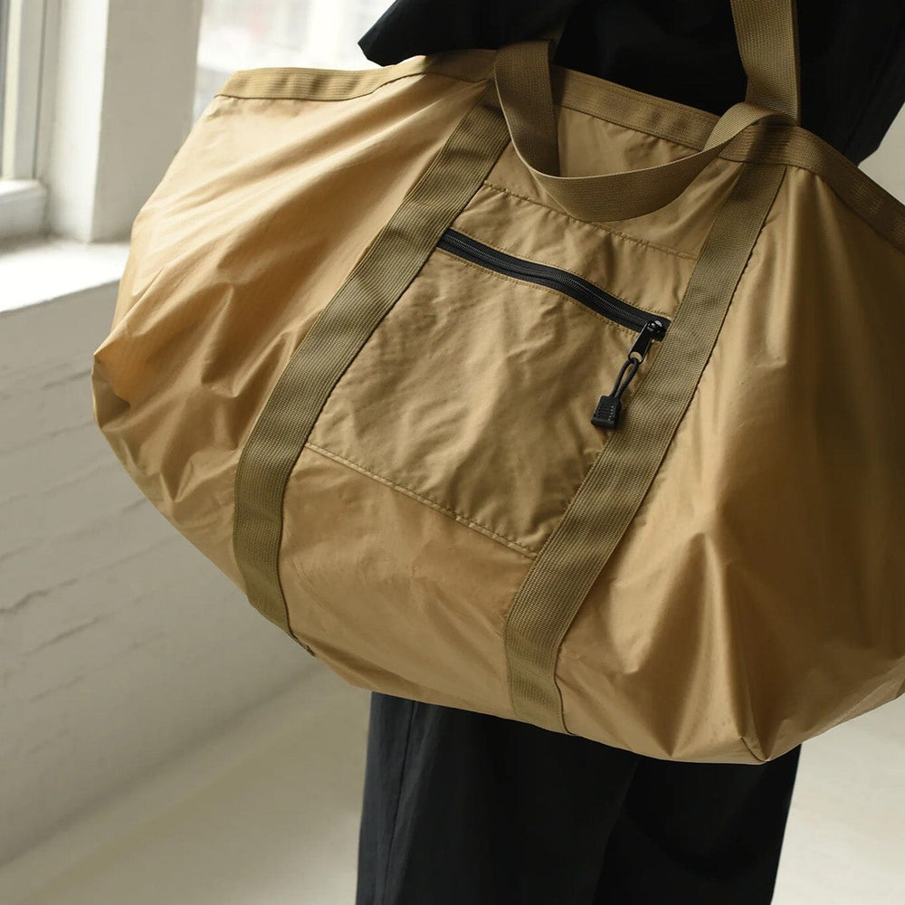 
                  
                    Person holding a light brown duffel bag with a strap over shoulder.
                  
                